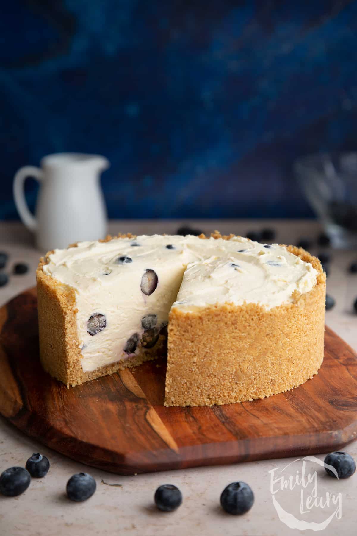 Blueberry cheesecake pie on a wooden board. One slice has been taken.