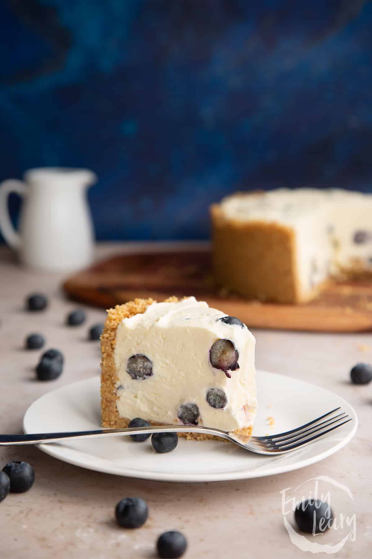 Slice of Blueberry cheesecake pie on a white plate with a fork. Some has been eaten. 