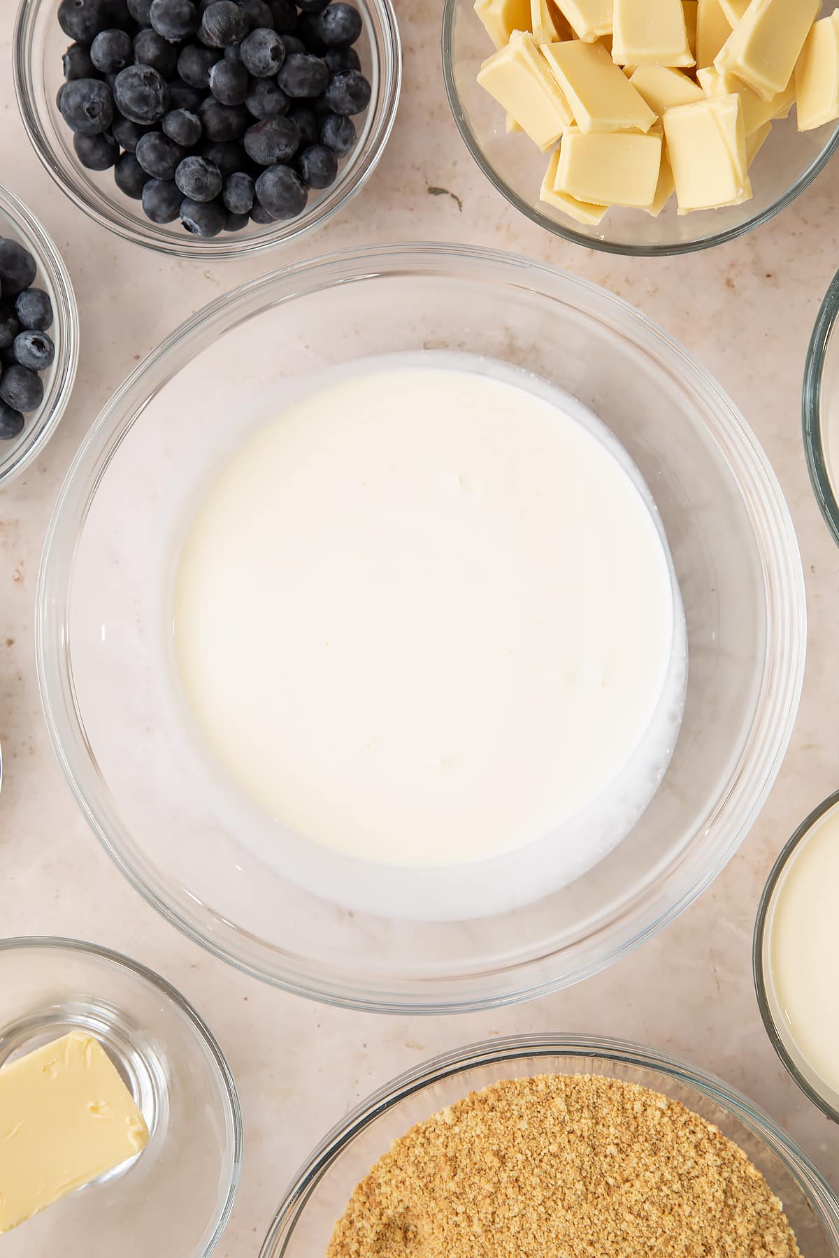 Cream in a bowl. Ingredients to make blueberry cheesecake pie surround the bowl.