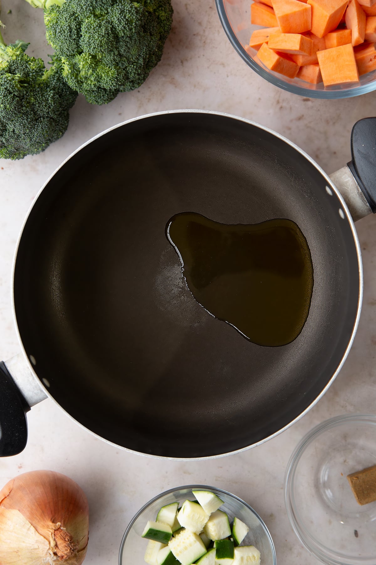 Overhead shot of oil in a pan with ingredients for the broccoli and sweet potato soup surrounding it.