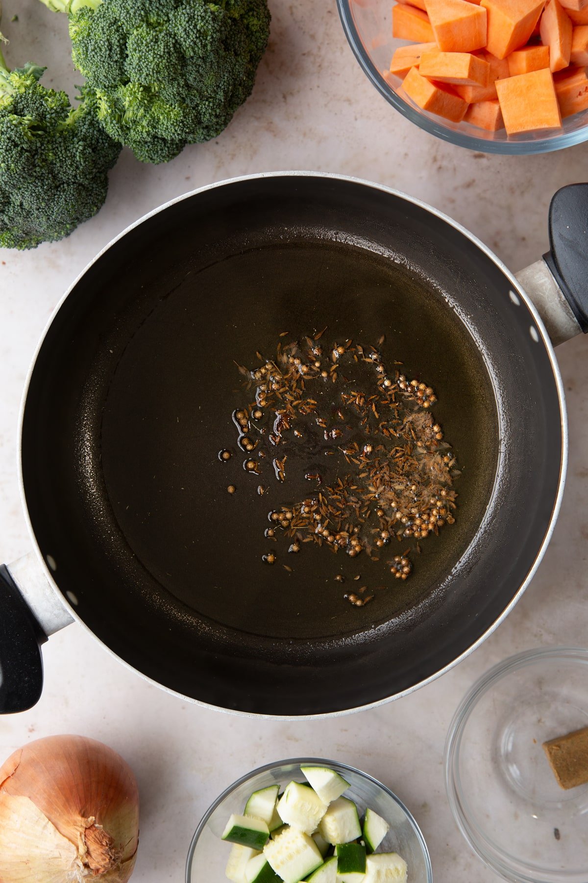 Adding cumin and corriander seeds to the pan of oil. 