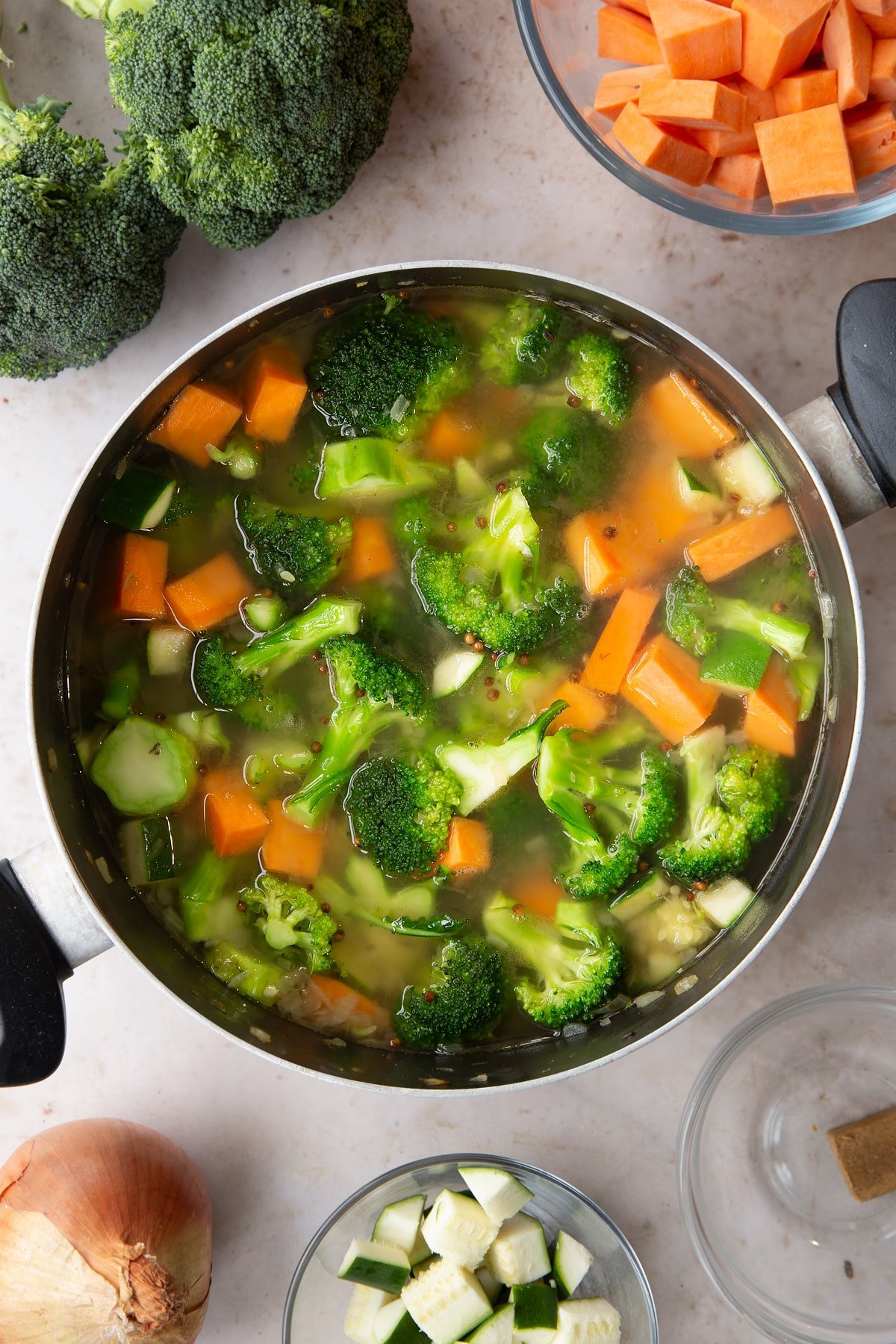 Adding stock to the pan of broccoli and sweet potato soup ingredients.