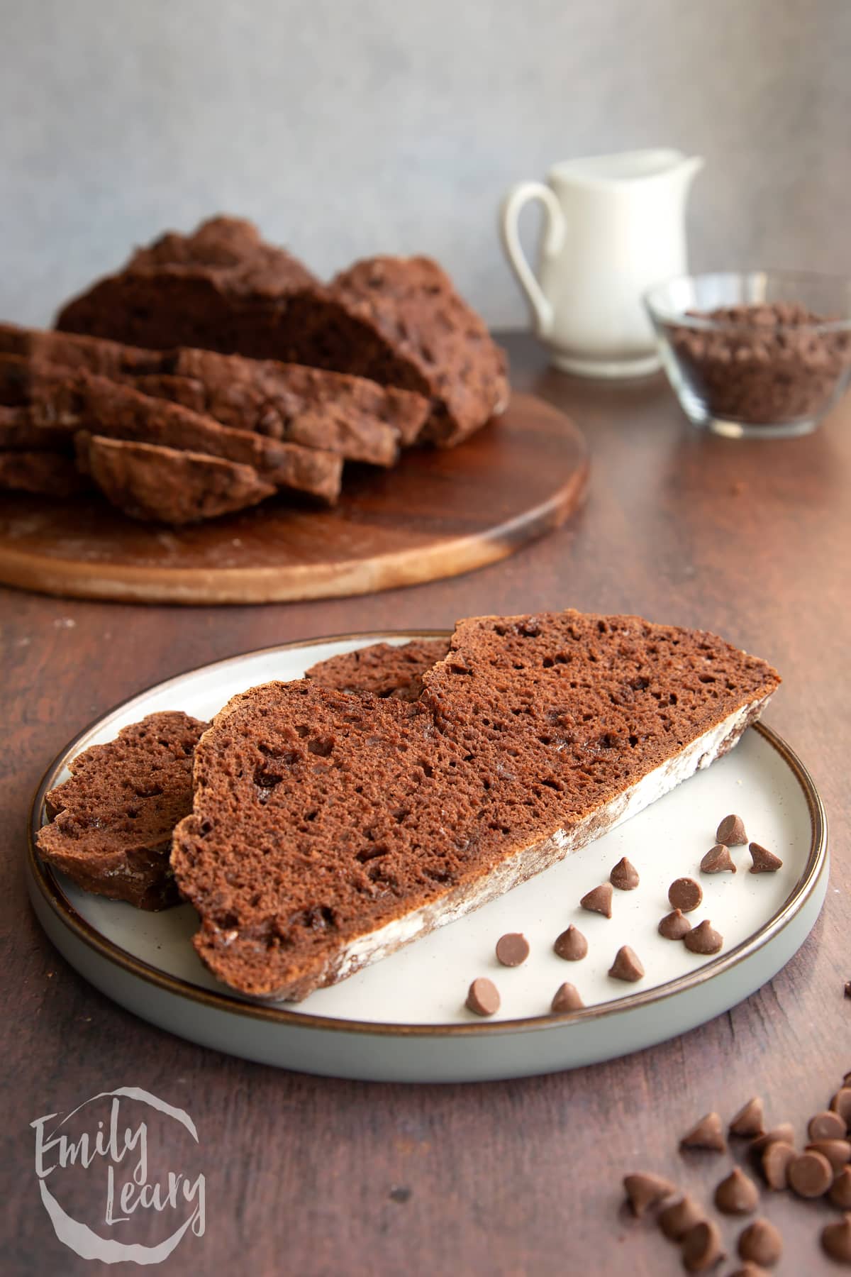A finished slice of chocolate soda bread served on a decorative plate with the remaining chocolate soda bread in the background on a wooden board.
