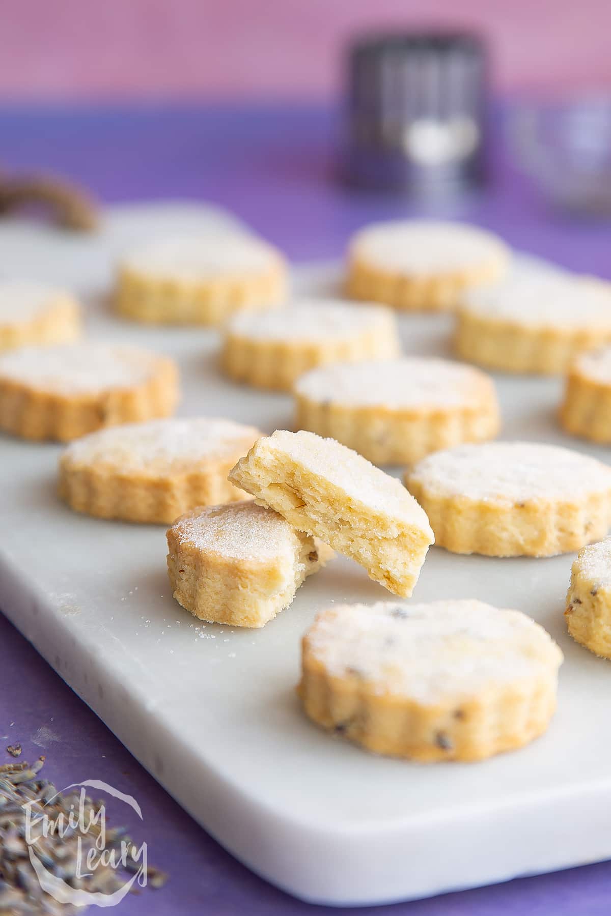 Lavender shortbread cookies on a marble board. One is broken in half.