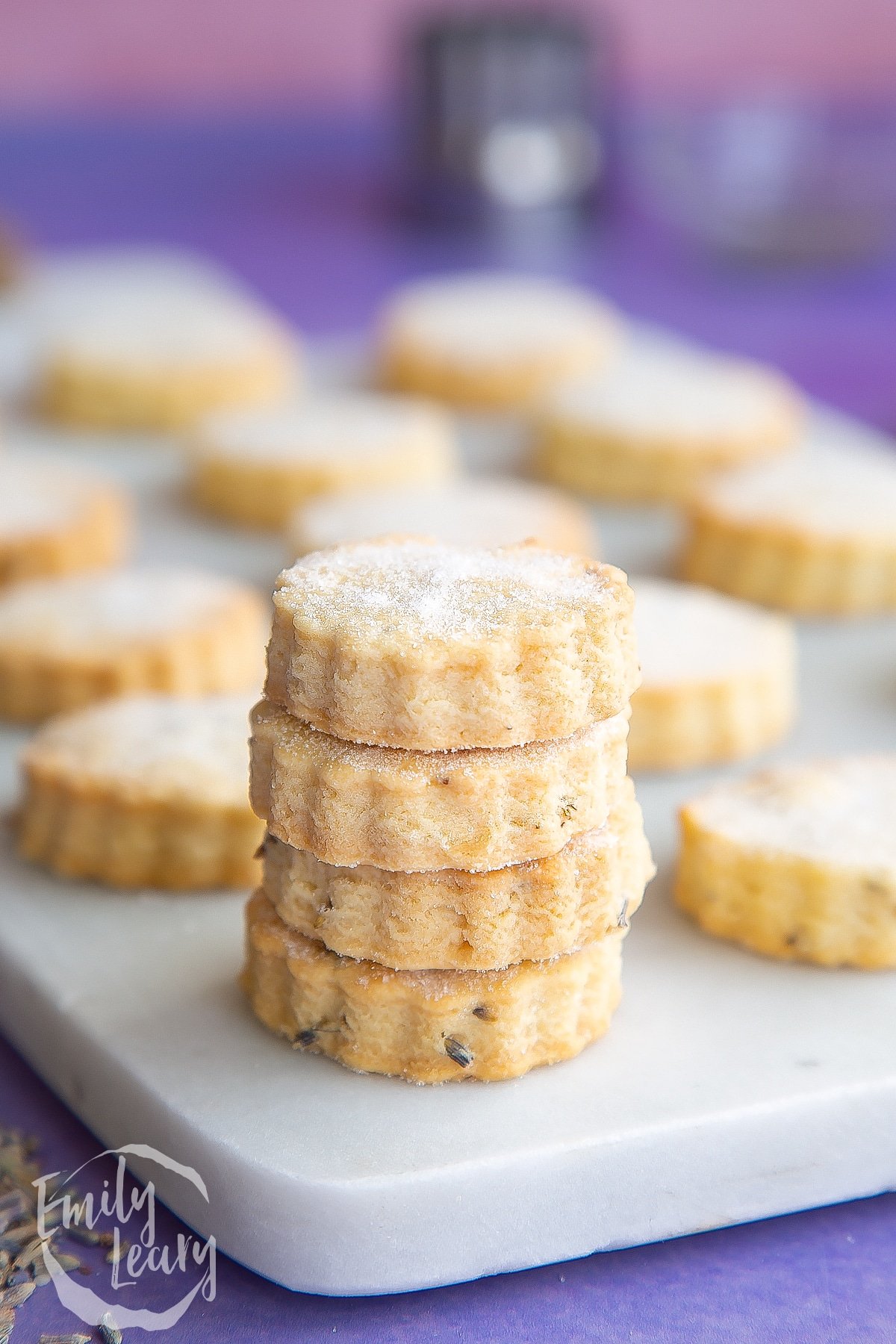 Lavender shortbread cookies stacked on a white marble board.