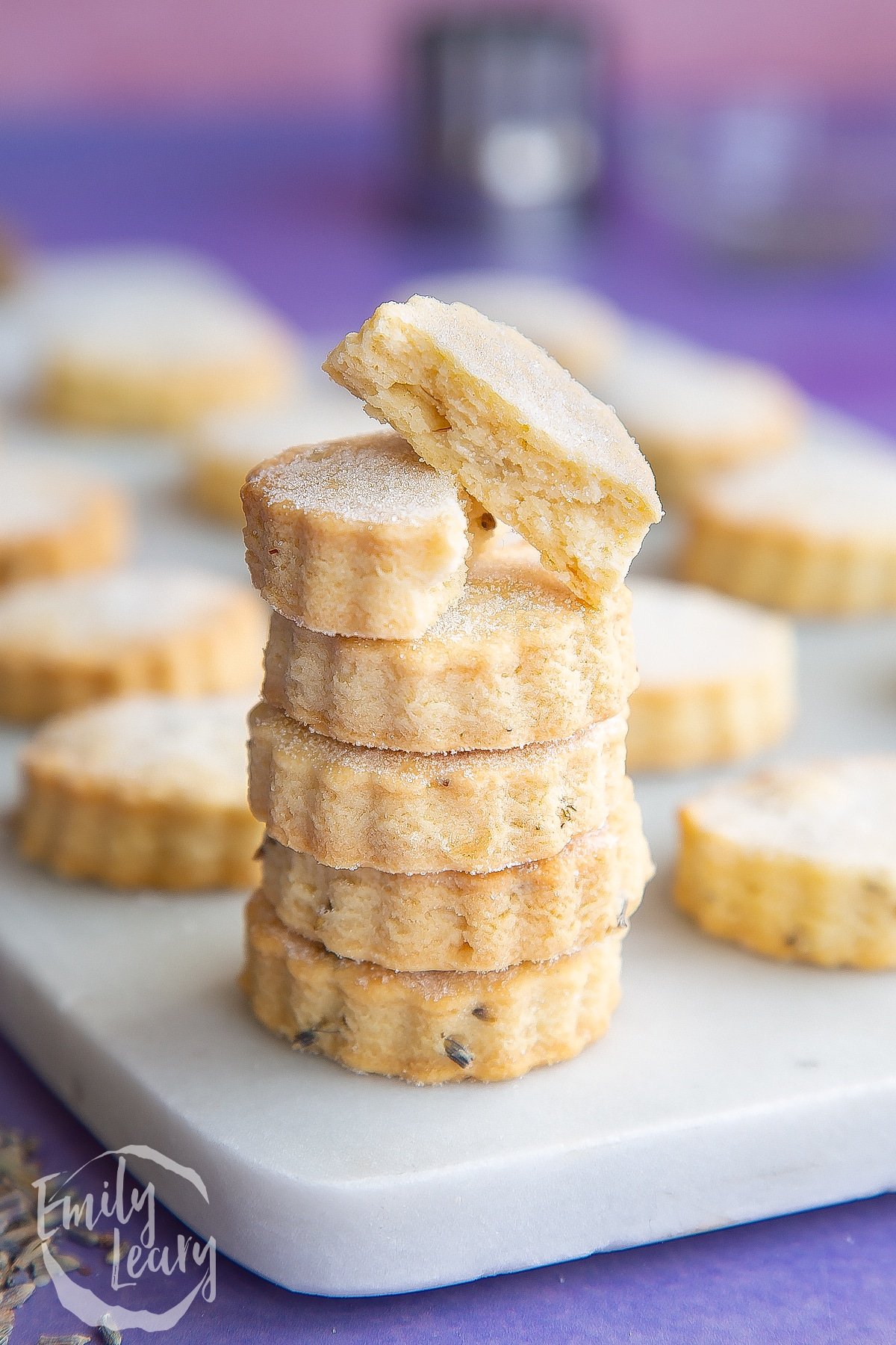 Lavender shortbread cookies in a stack on a marble board. The top one is broken in half.