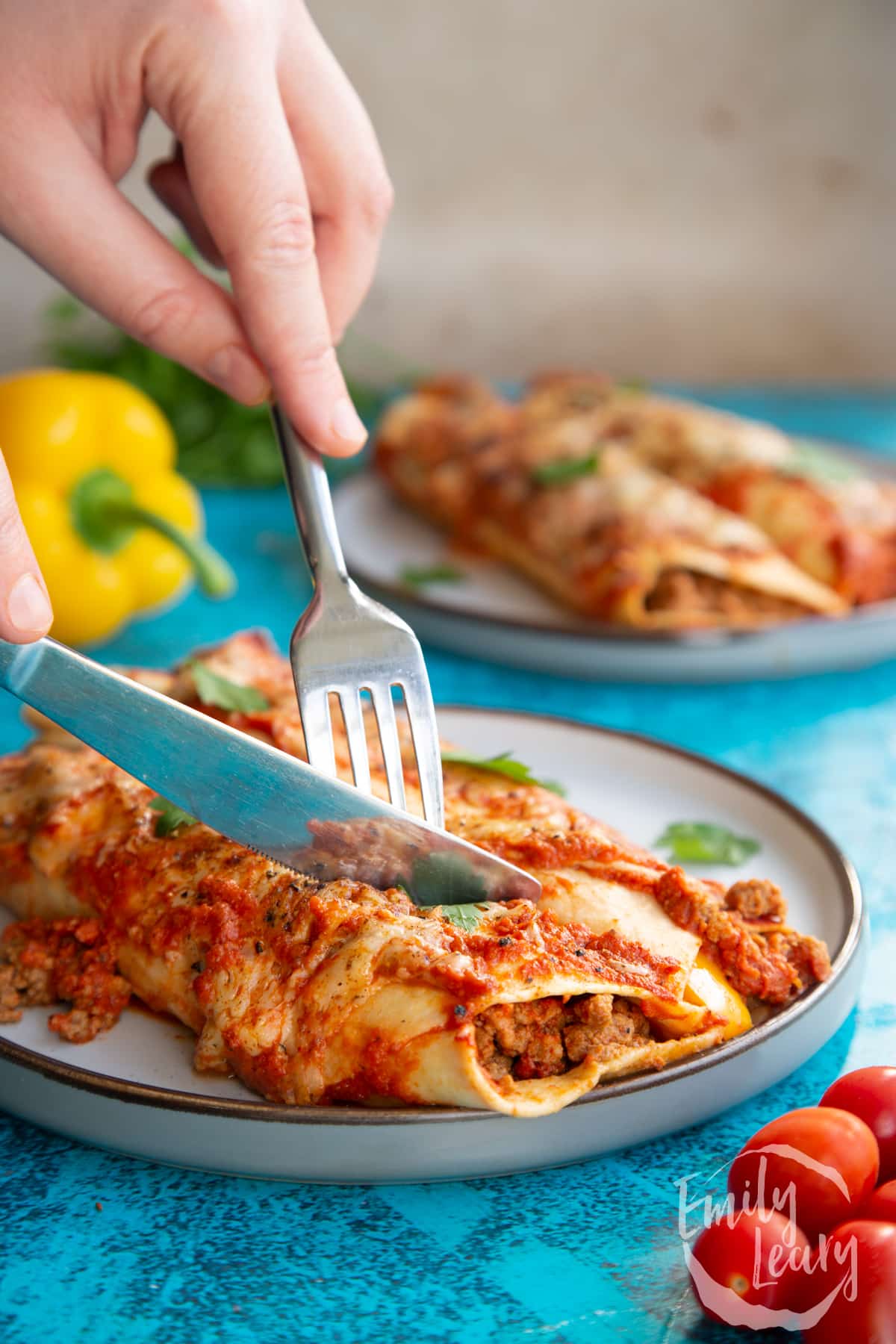 Quorn mince enchiladas served on a grey plate. Hands cut into them with a knife and fork.