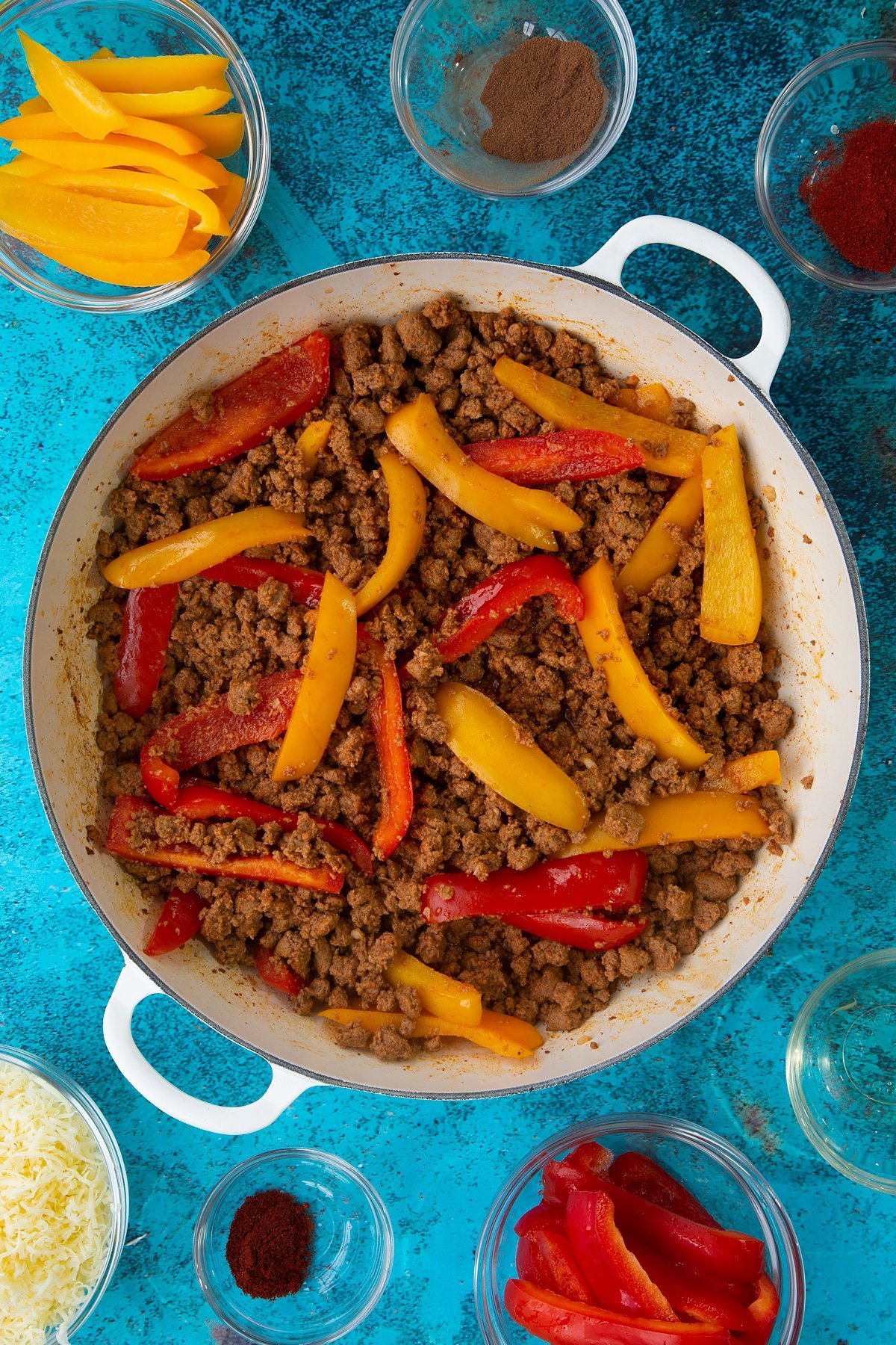 Quorn mince enchilada filling in a large white pan. Ingredients to make Quorn mince enchiladas surround the pan.