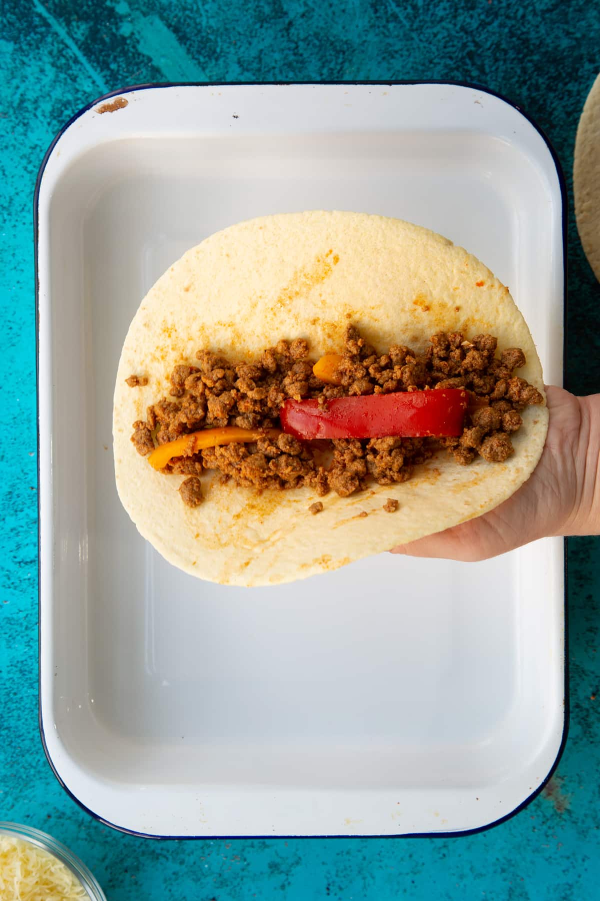 Hand holding a tortilla with Quorn mince enchilada filling on top.