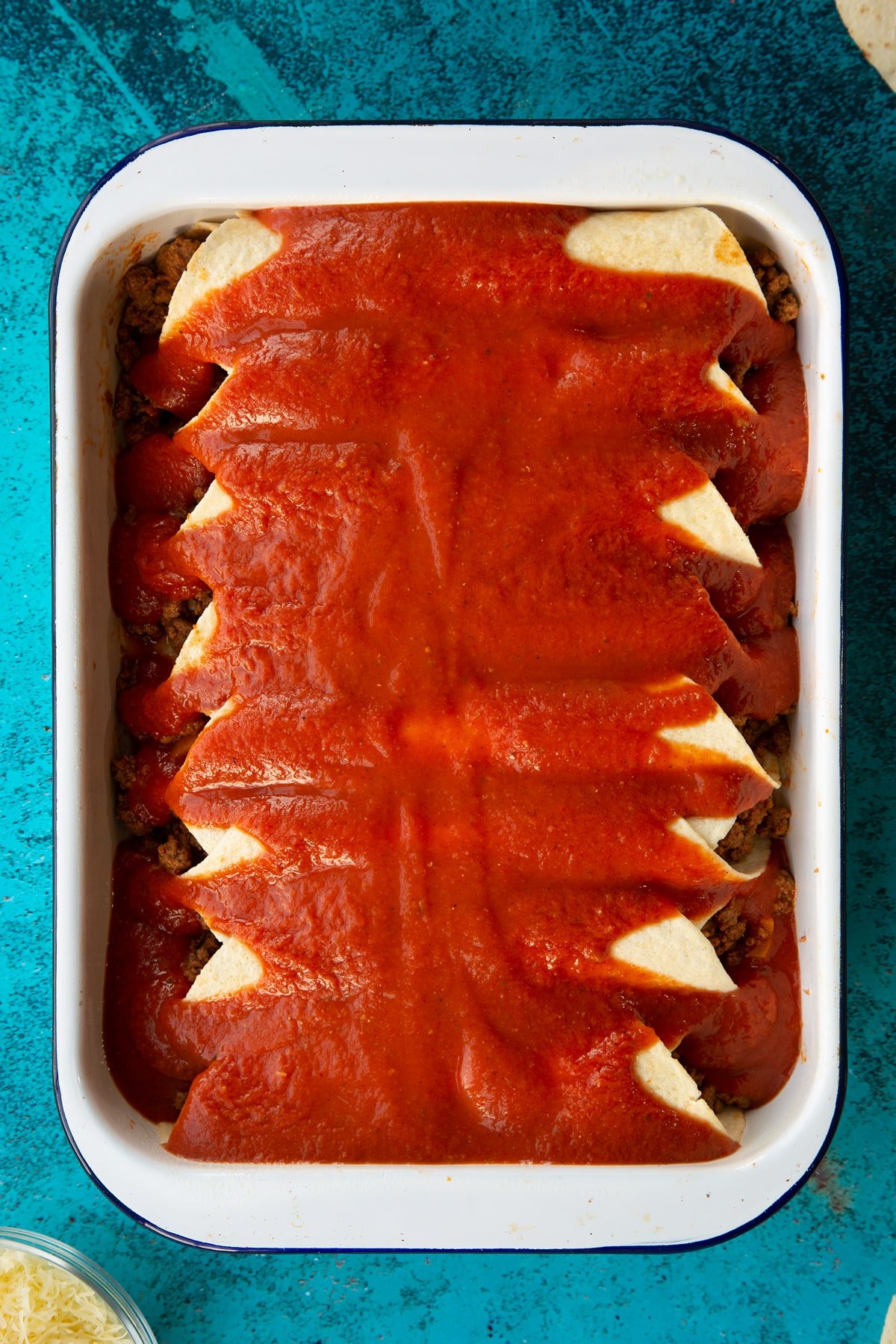A tray of tortillas filled with Quorn mince enchilada filling, with enchilada sauce on top.