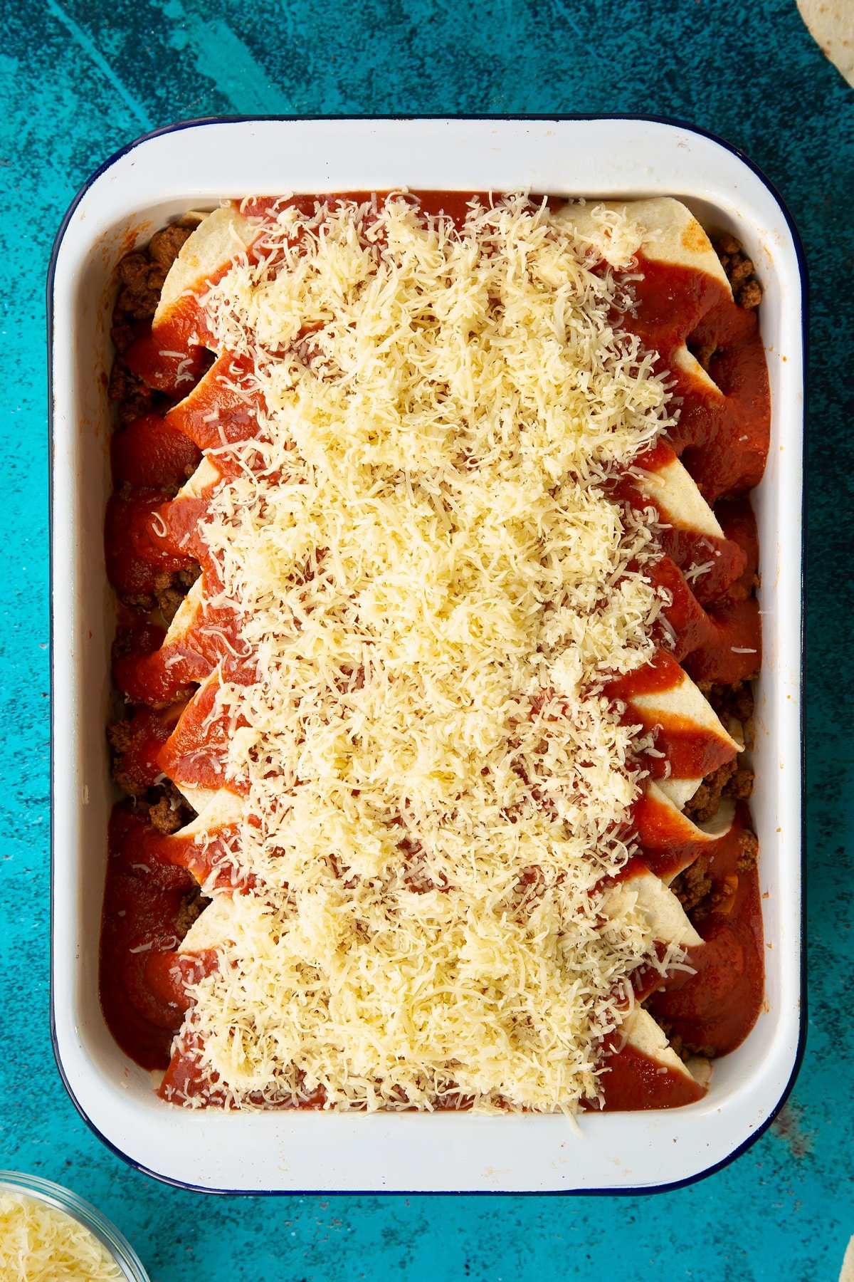 A tray of tortillas filled with Quorn mince enchilada filling, with enchilada sauce and cheese on top.
