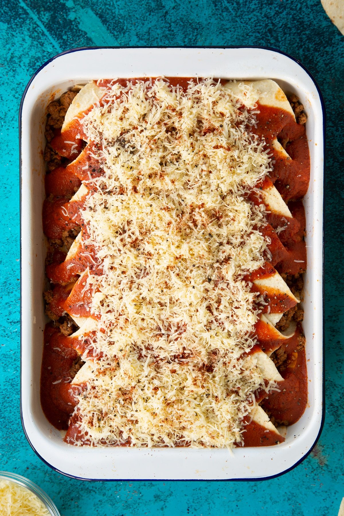 A tray of tortillas filled with Quorn mince enchilada filling, with enchilada sauce, cheese and seasoning on top.