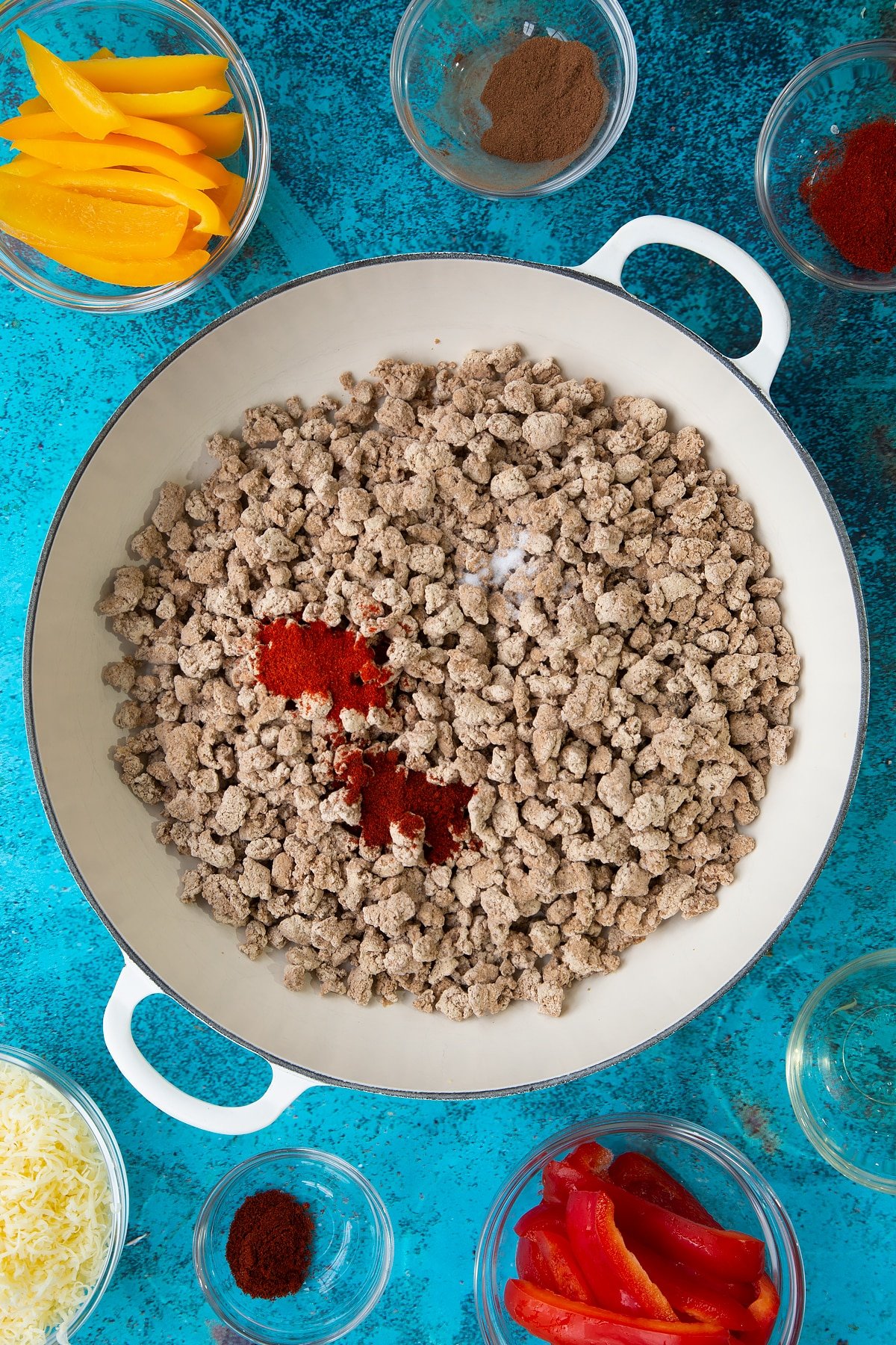 Frozen Quorn mince, spices and garlic in a large white pan. Ingredients to make Quorn mince enchiladas surround the pan.