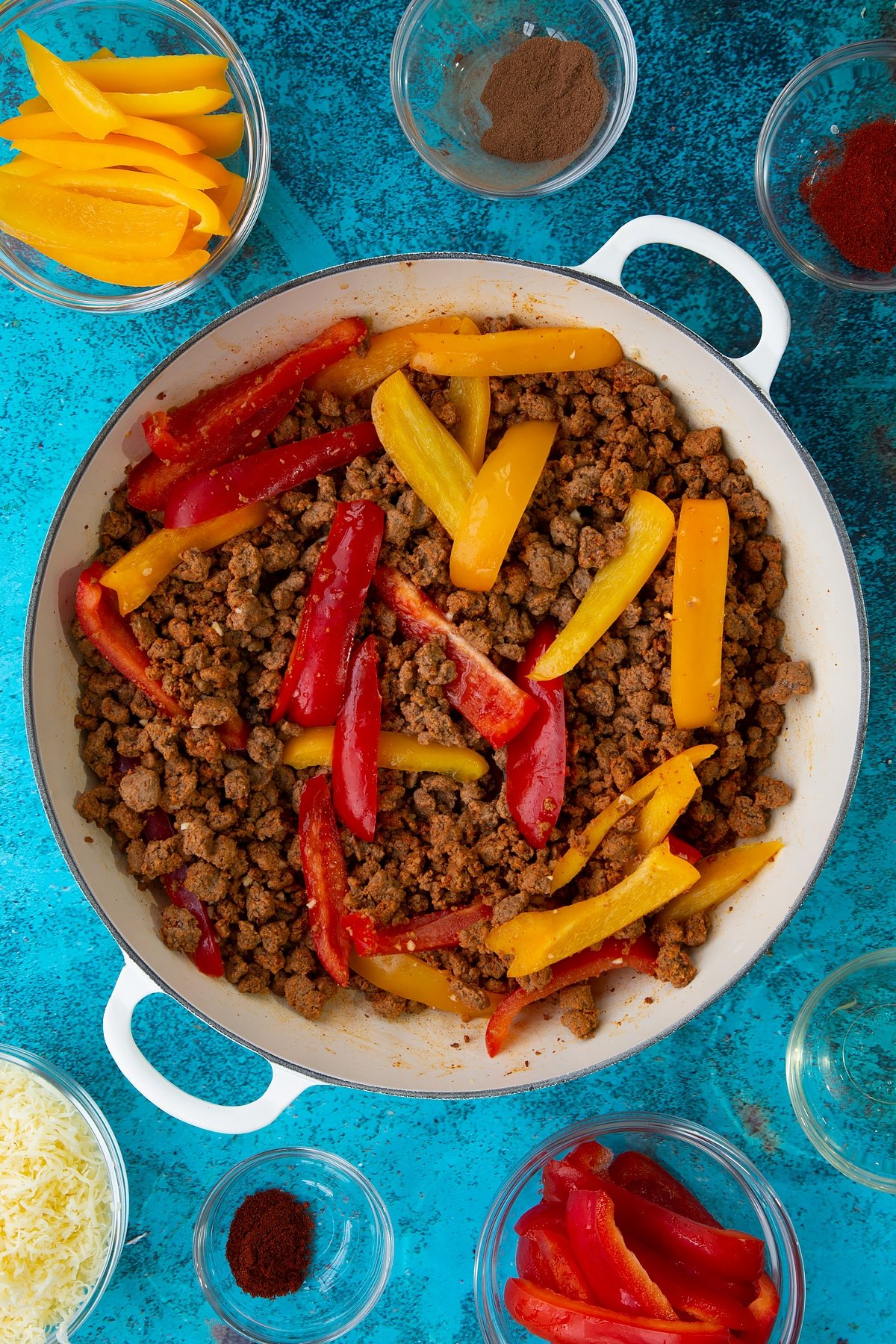 Quorn mince and peppers fried in garlic and spices in a large white pan. Ingredients to make Quorn mince enchiladas surround the pan.