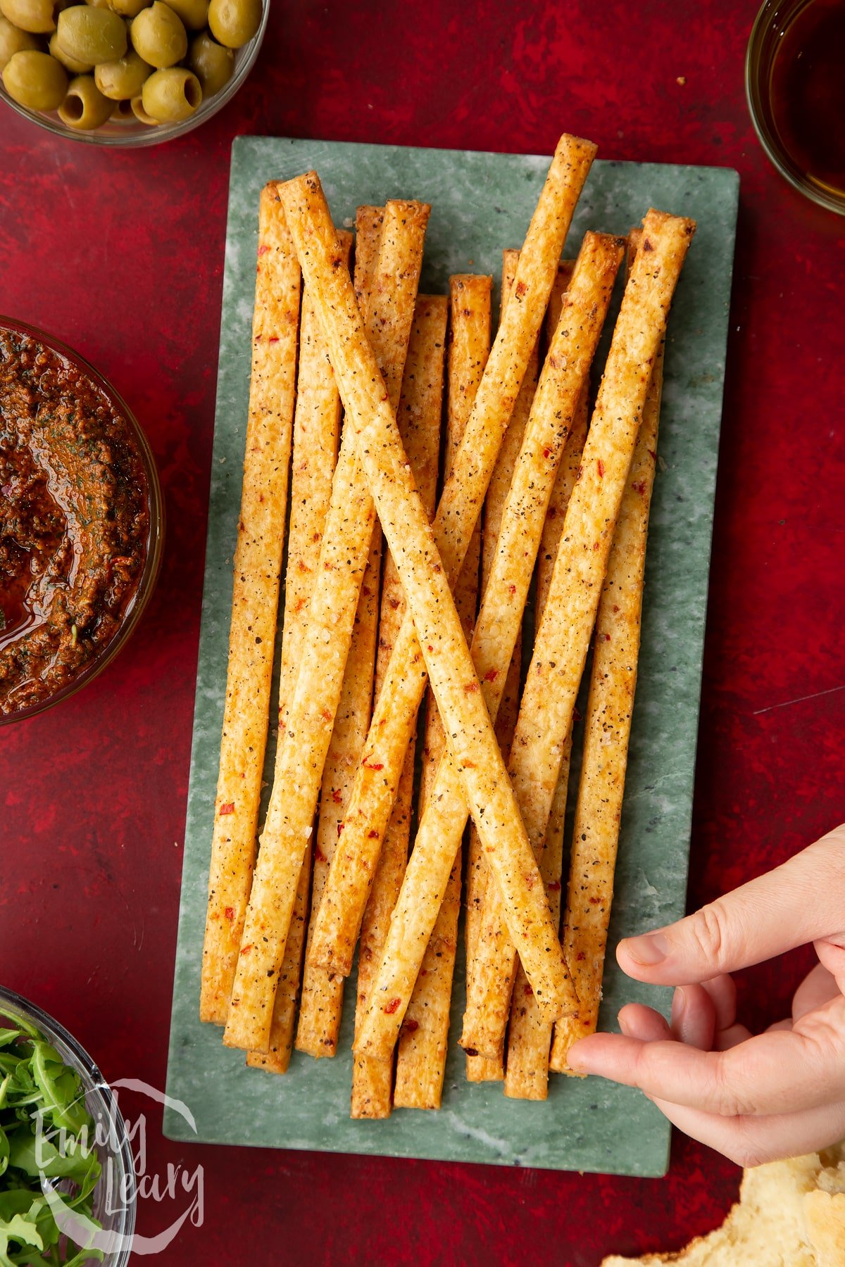 Overhead shot of the finished spicy cheese straws with a hand reaching in to grab one.