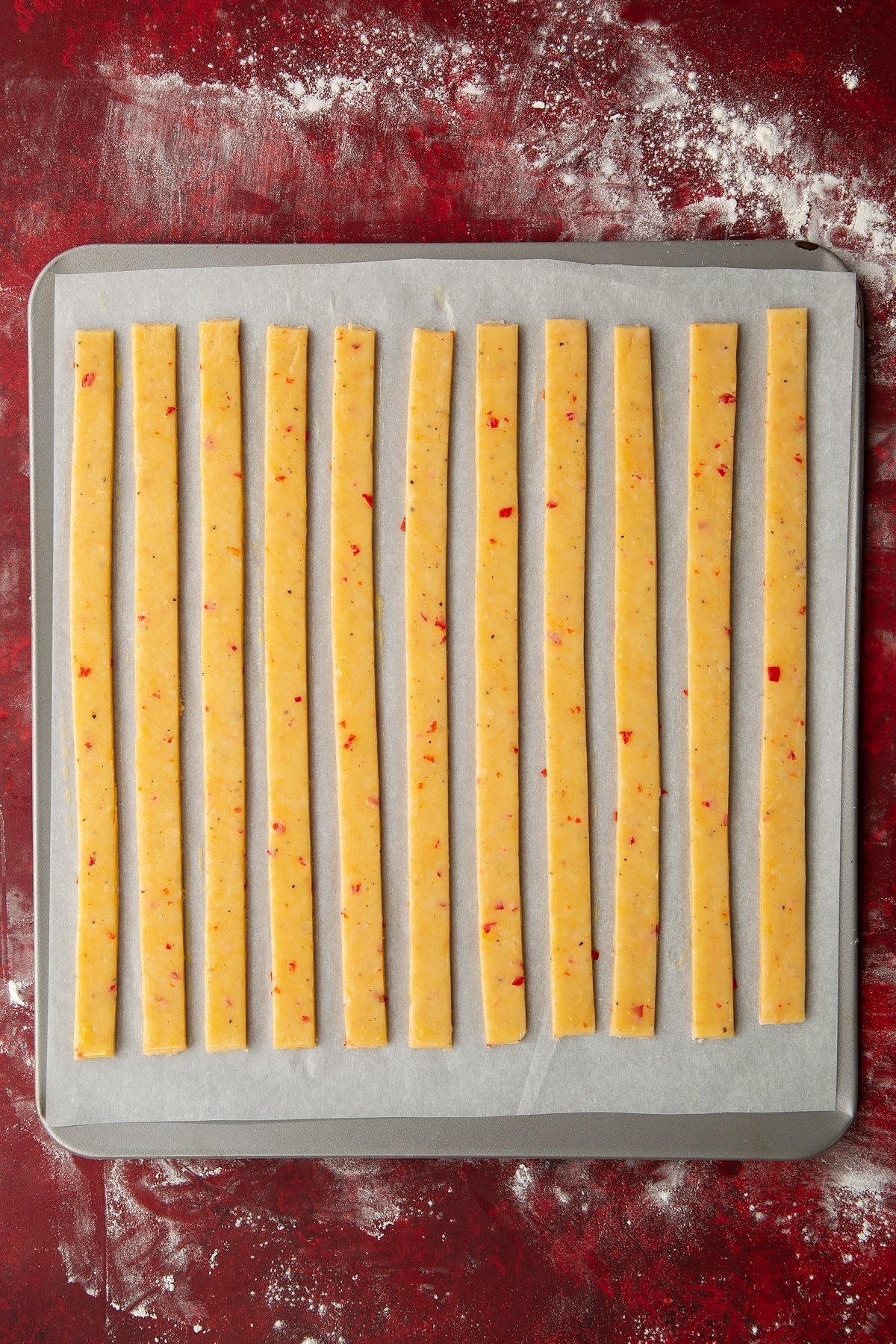 Overhead shot of the raw spicy cheese straws being lightly baste with raw egg.