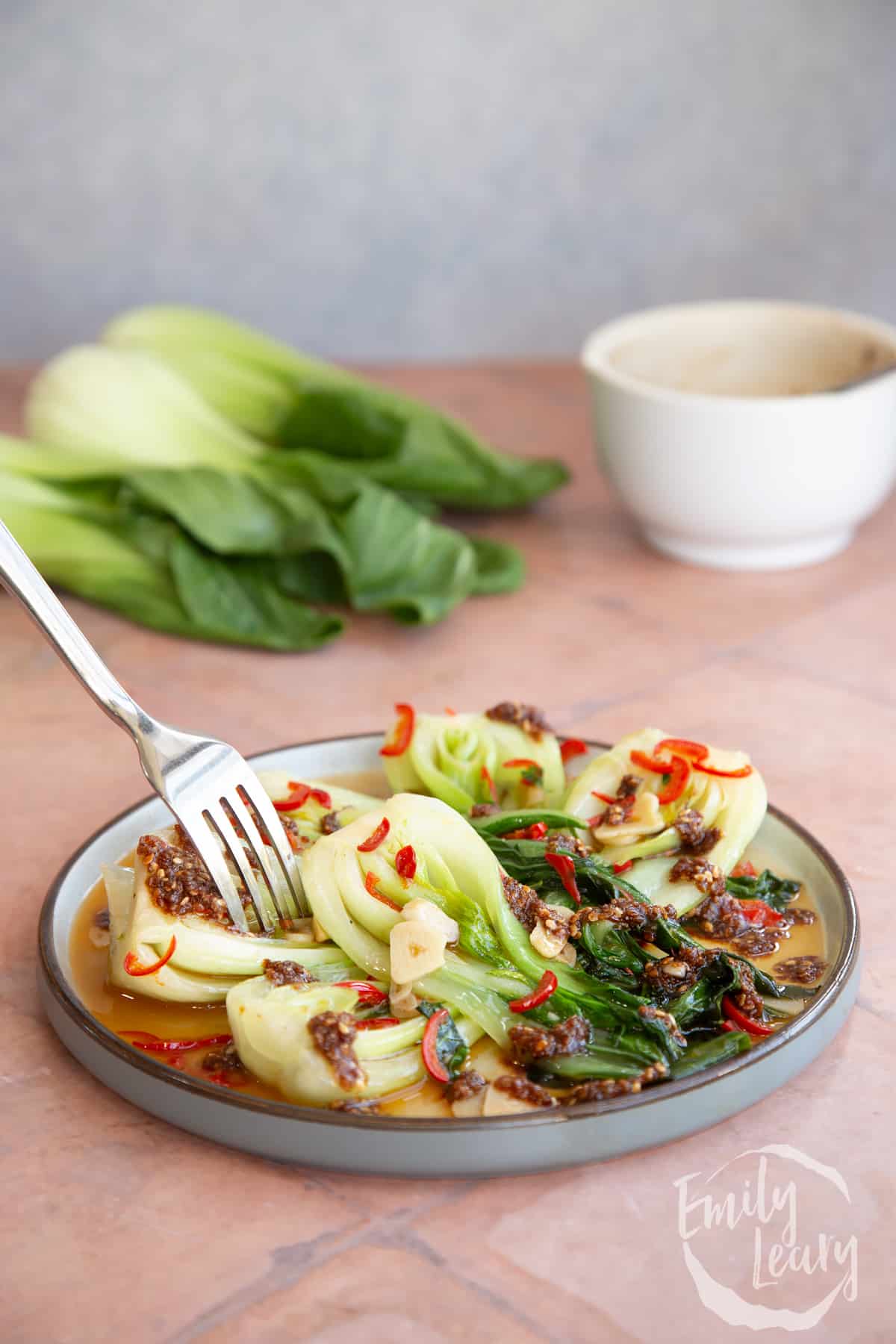 Side on shot of the spicy pak choi served on a plate with a fork coming in from the top.