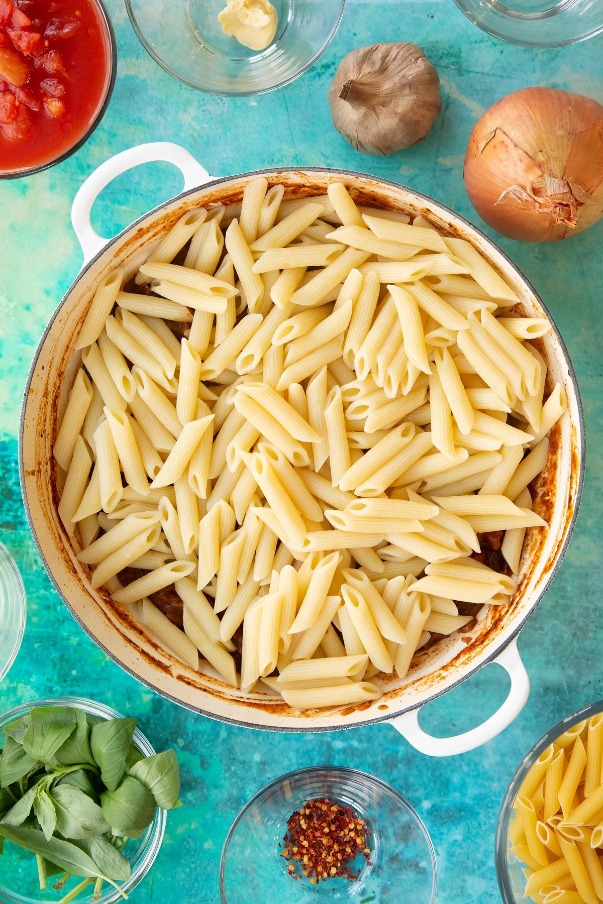 Overhead shot of the pasta being added to the pan of black garlic pasta ingredients.