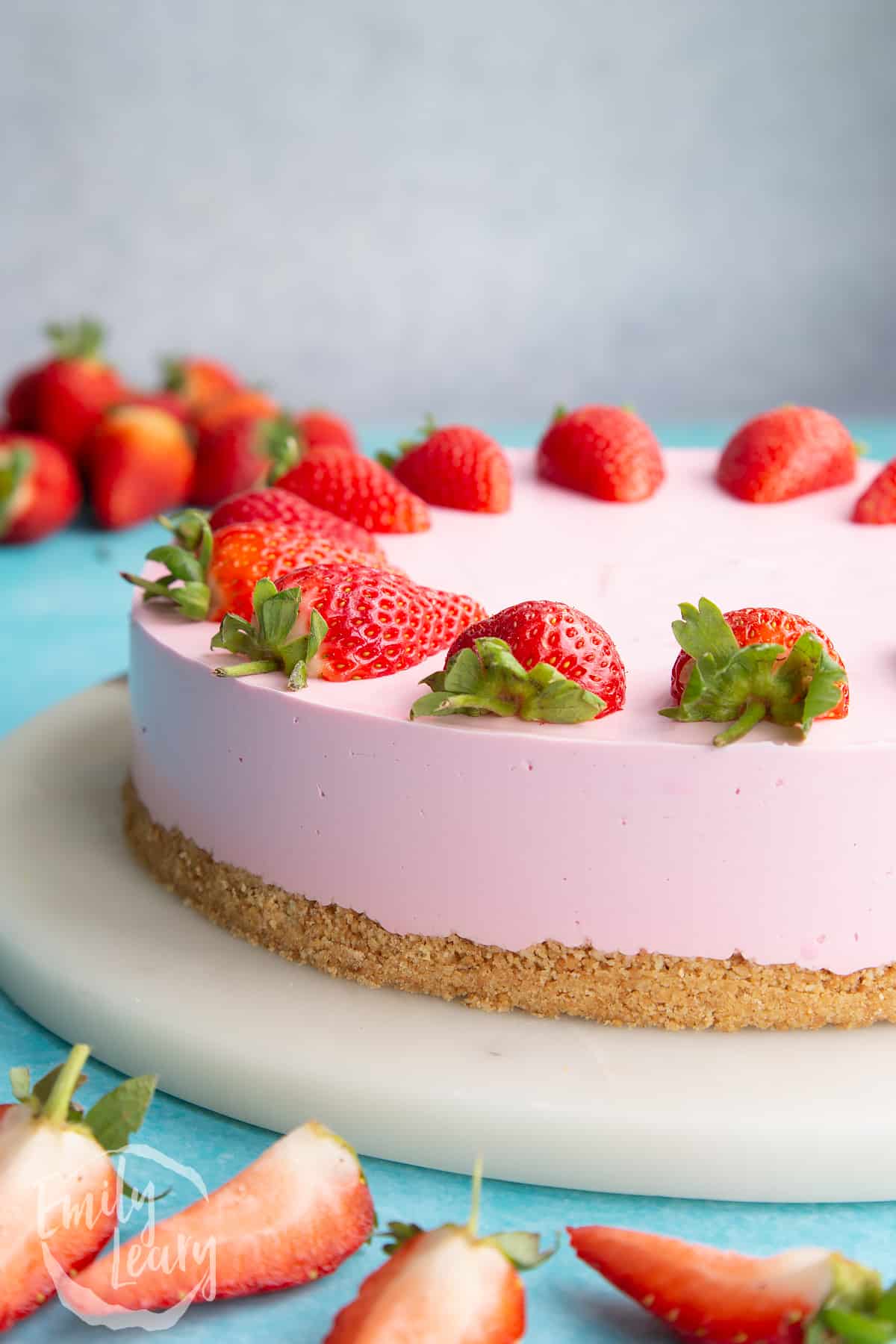 A pink jello cheesecake topped with a strawberry halves on a white marble board.