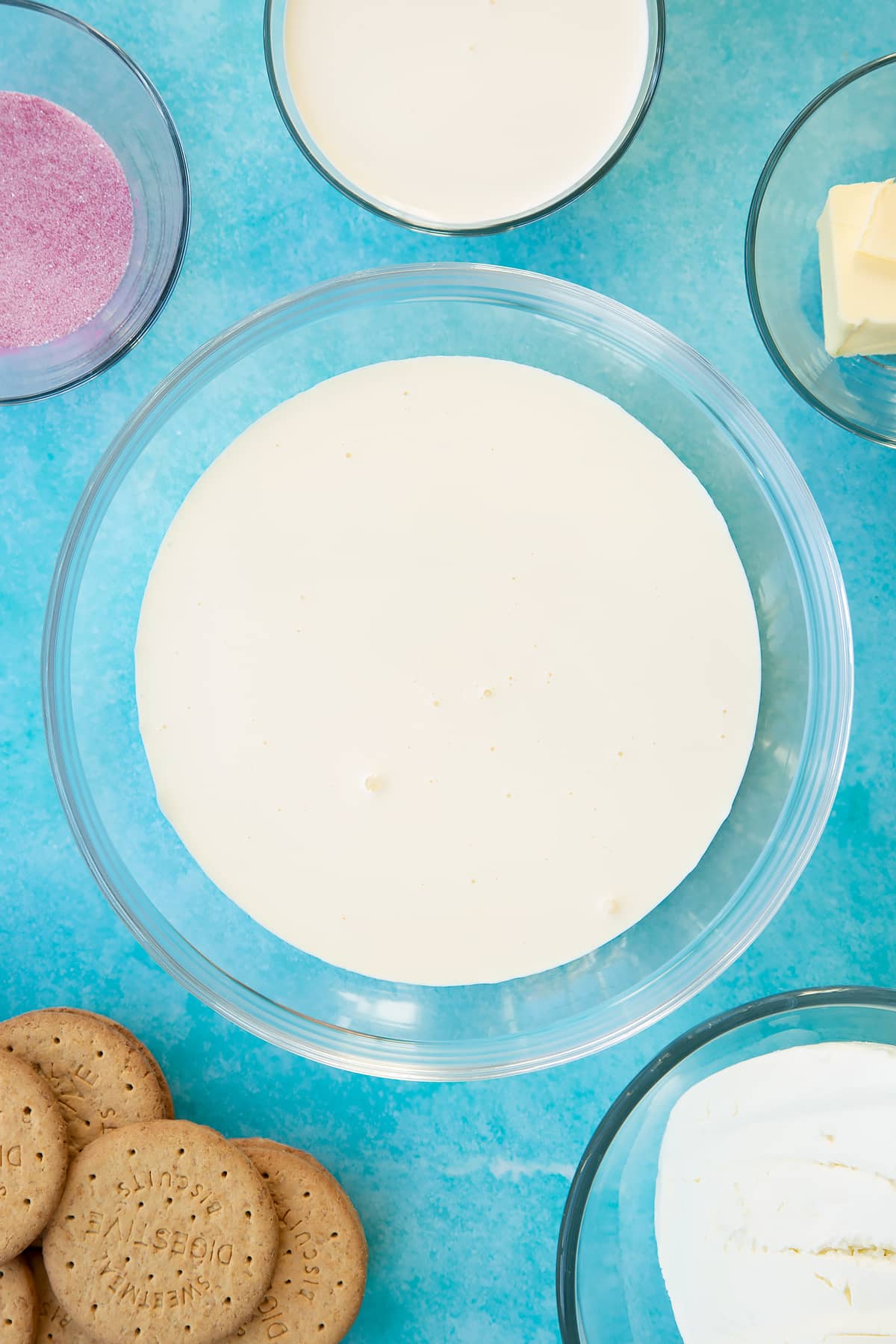 Double cream in a glass bowl. Ingredients to make jello cheesecake surround the bowl.