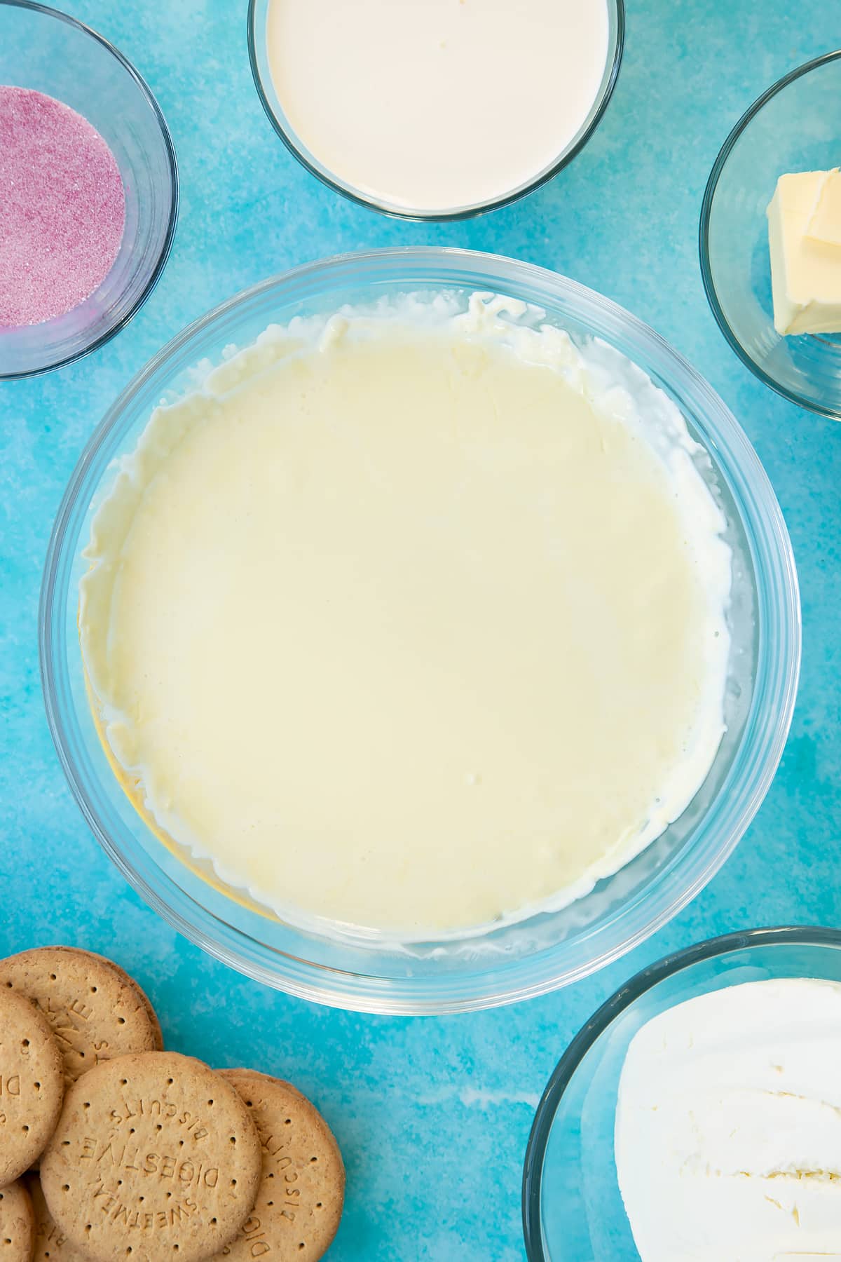 Hot double cream in a glass bowl. Ingredients to make jello cheesecake surround the bowl.