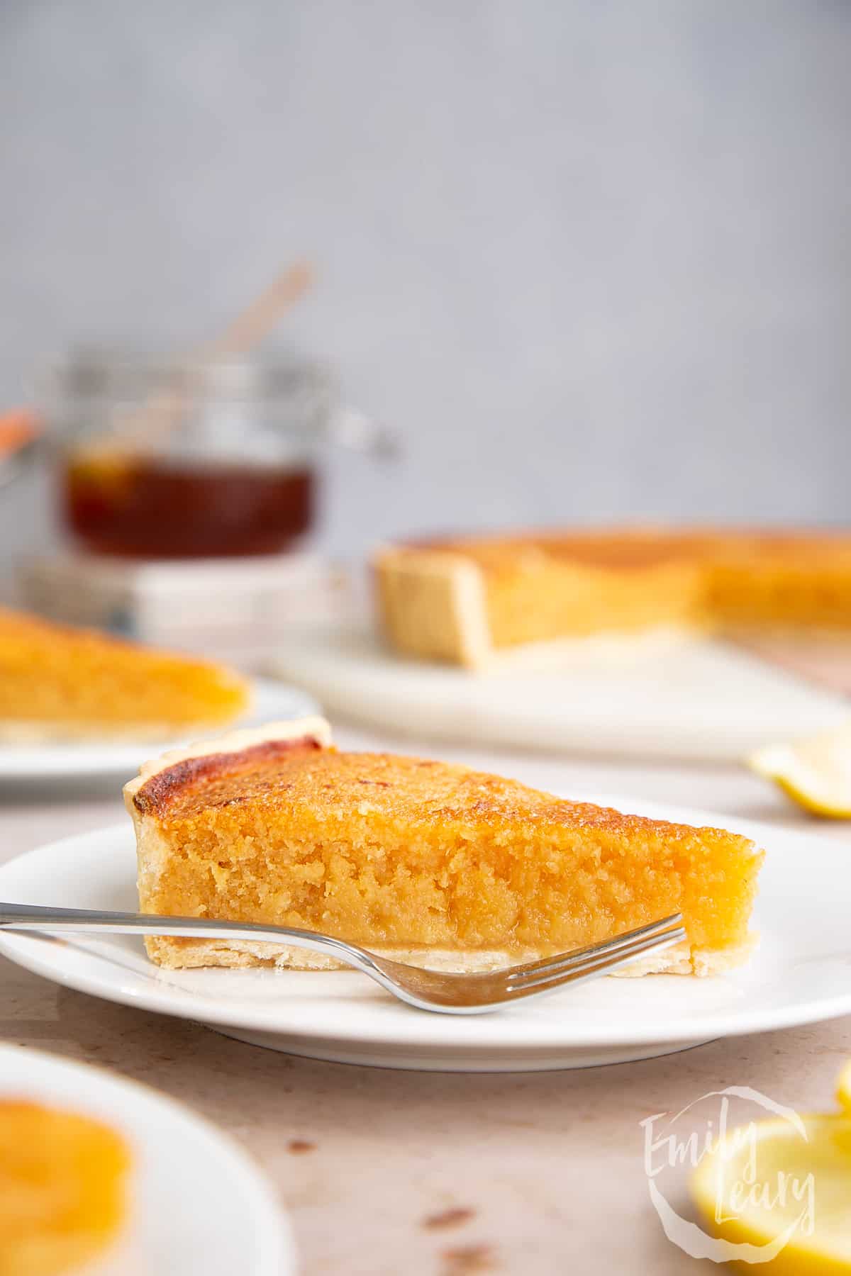 A side on shot of a lemon treacle tart slice on a white plate with a fork on the side.