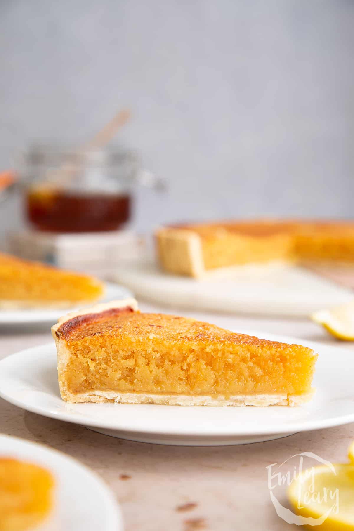 Side on shot of a slice of lemon treacle tart on a white plate.