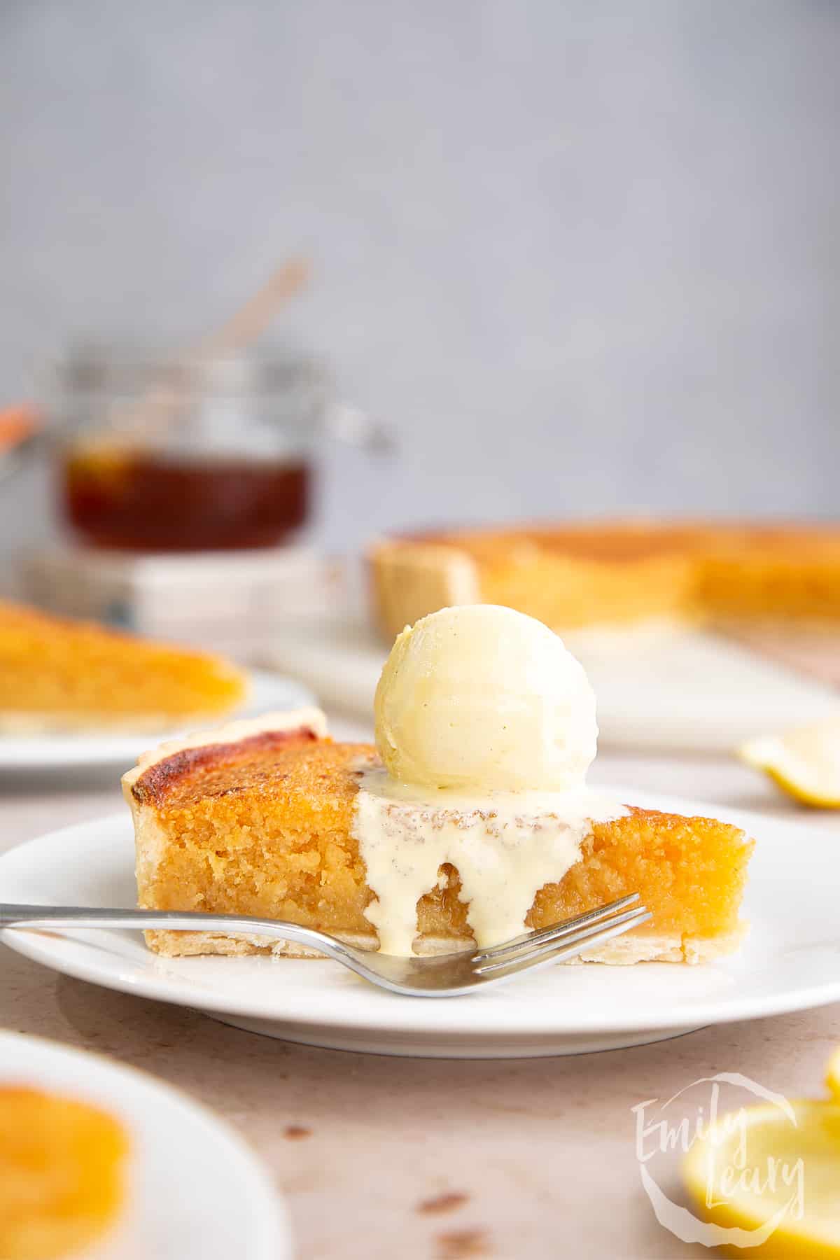 A slice of lemon treacle tart on a white plate with a scoop of ice-cream ontop.