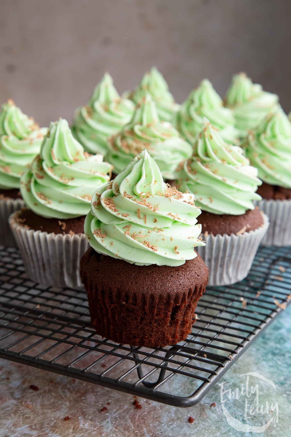 A batch of mint choc chip cupcakes cooling on a rack.