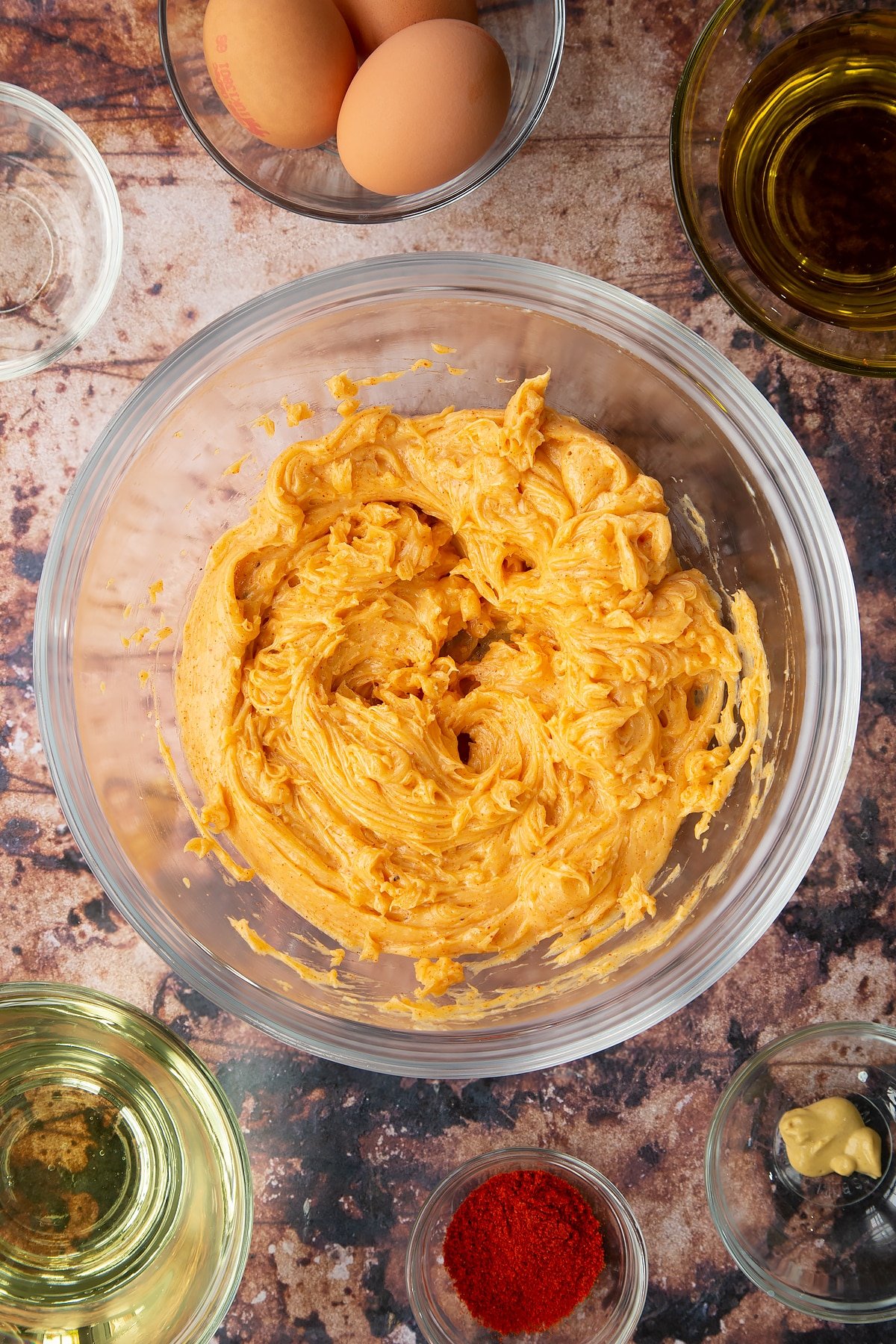 Thick paprika mayo in a bowl. Ingredients to make paprika mayo surround the bowl.