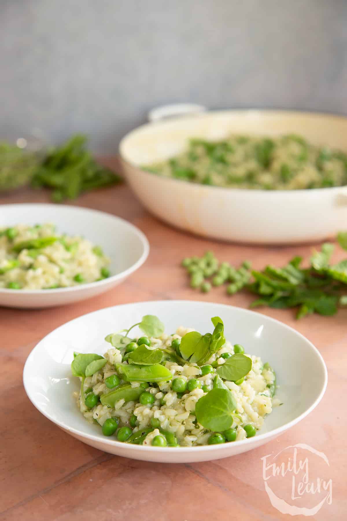 Side on shot of a bowl of pea and mint risotto with an additional plate in the background.