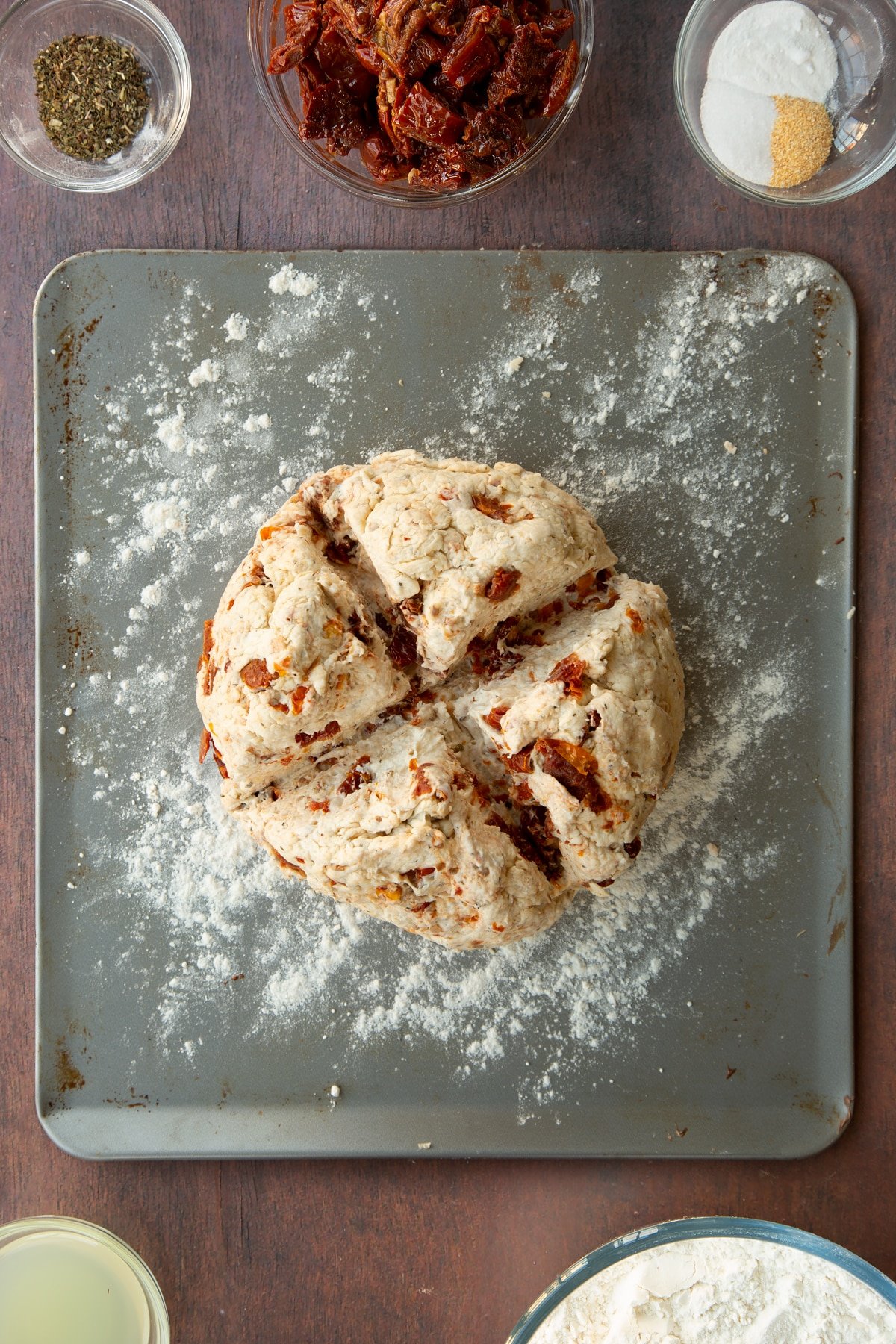 Sundried tomato soda bread dough with a cross cut into it on a baking tray.