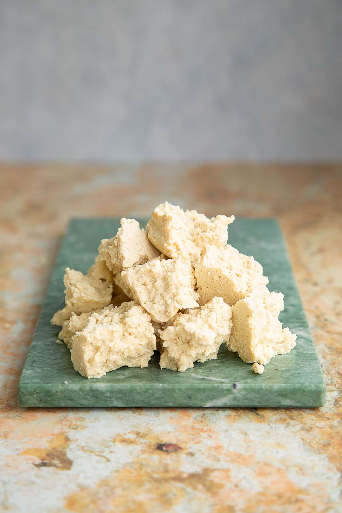 extra firm tofu defrosted and pulled tp pieces on a green marble board.