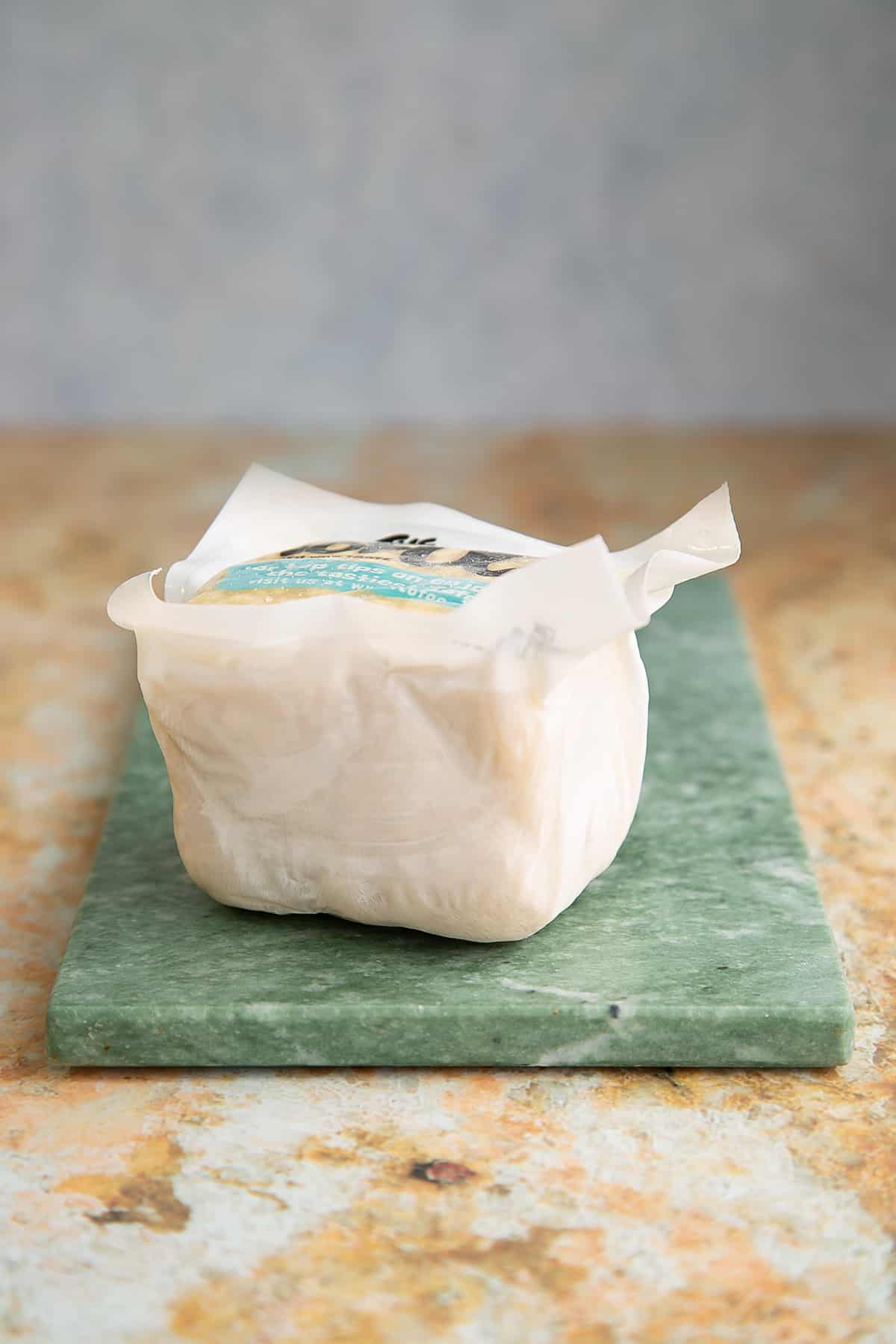 a block of tofu in a wrapper on a green marble board.