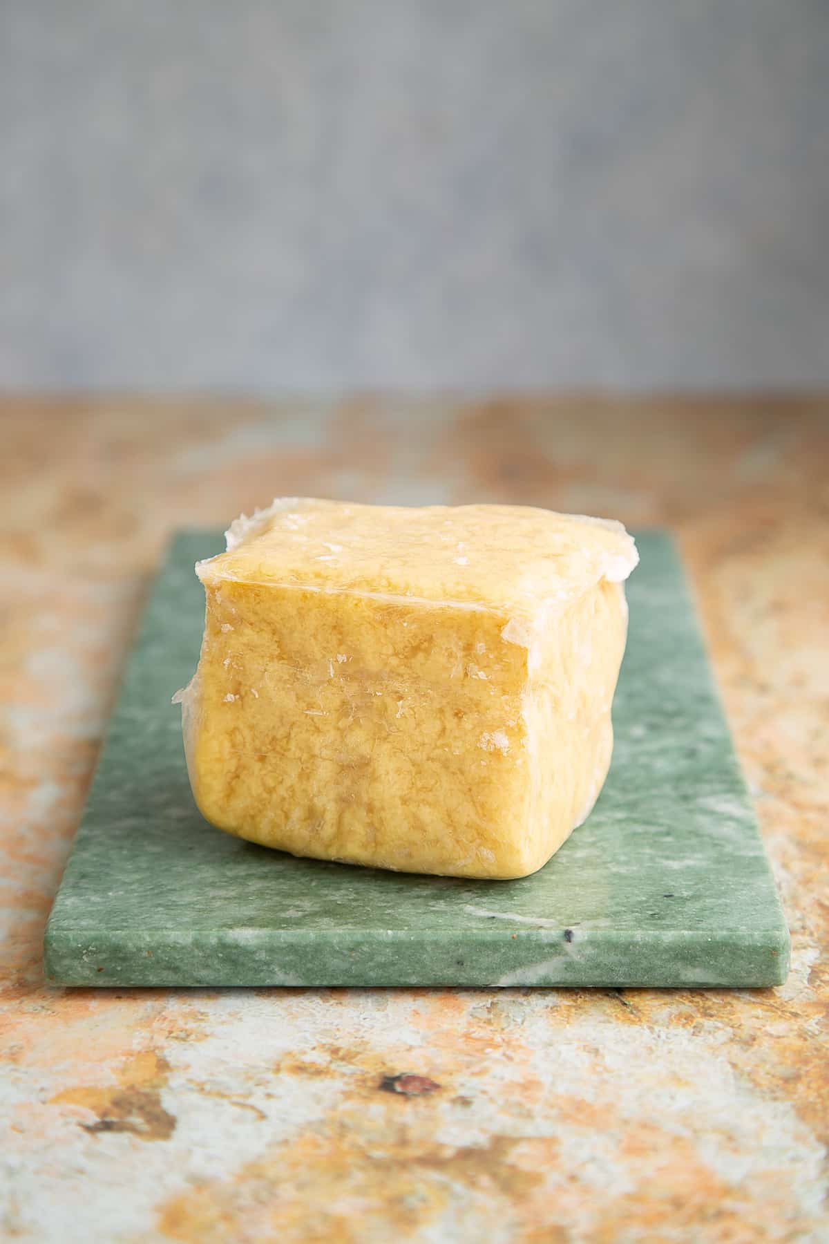 a block of frozen tofu on a green marble board.