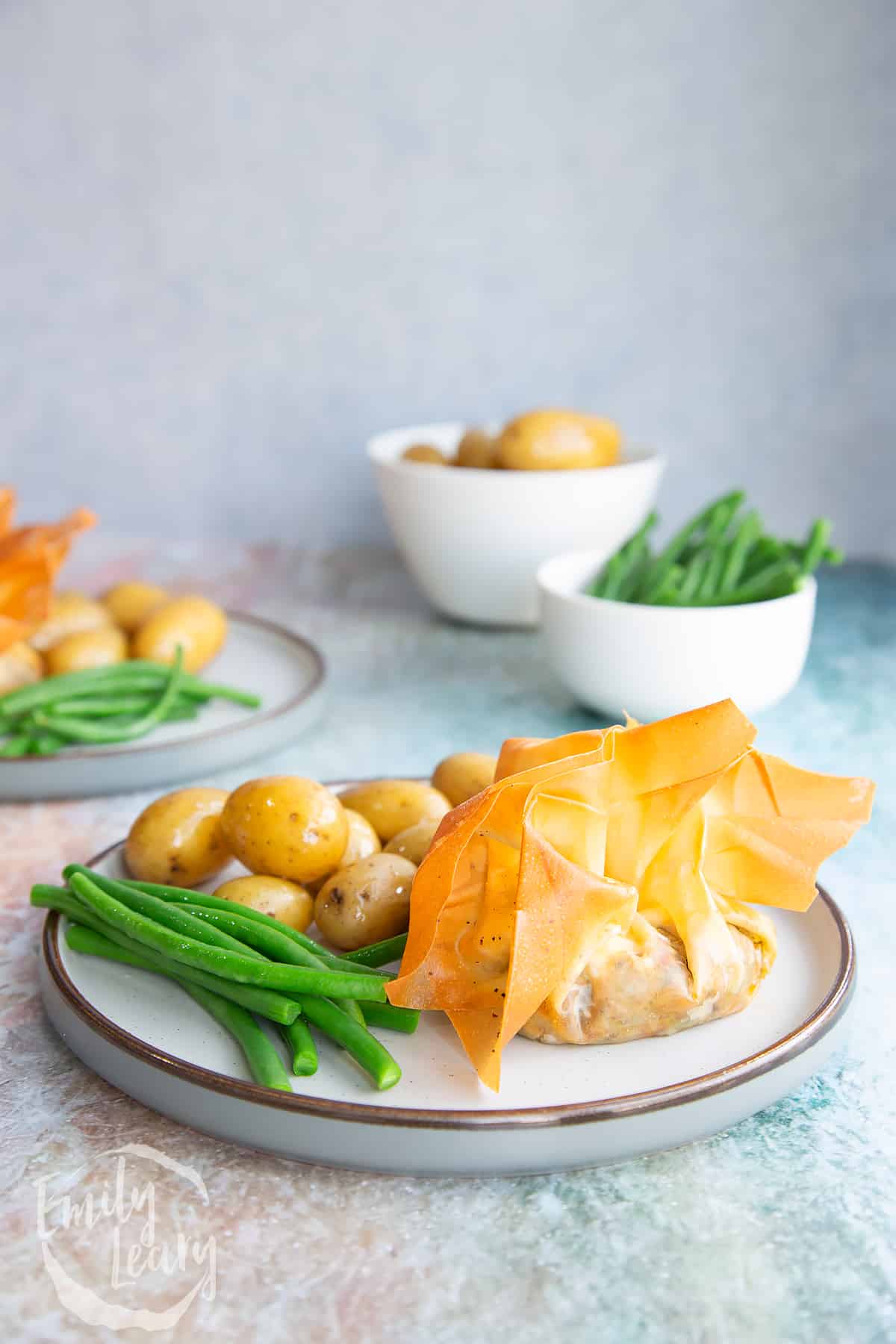 Goats cheese filo parcels on a white plate with green beans and small potatos.