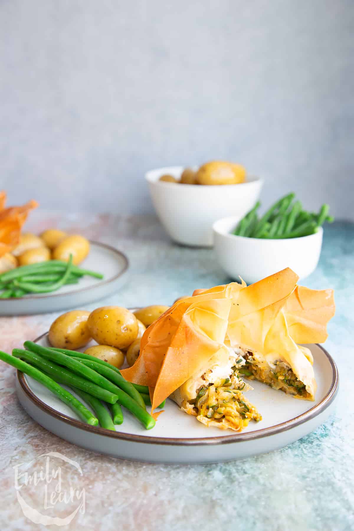 Goats cheese filo parcels on a white plate with green beans and small potatos.