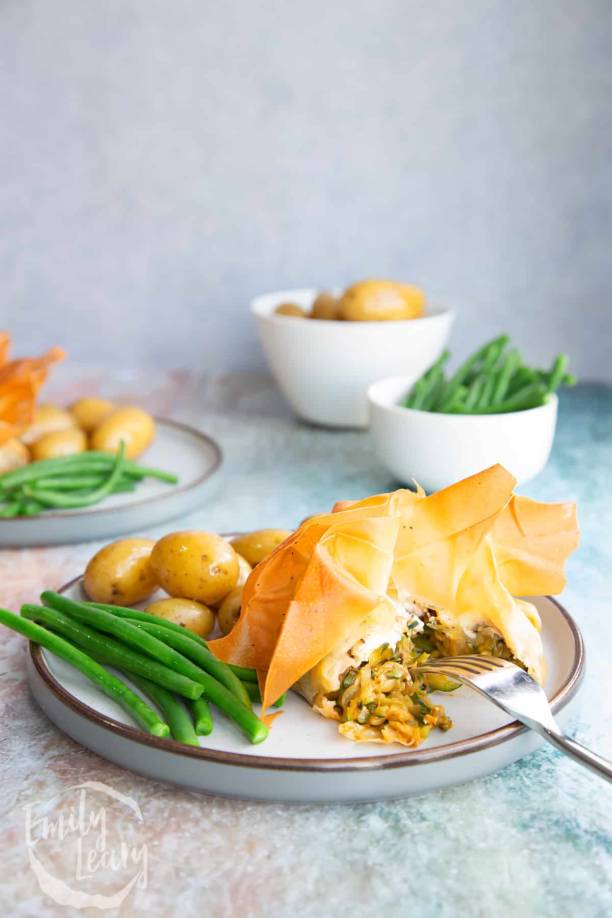 Goats cheese filo parcels on a white plate with green beans and small potatos.