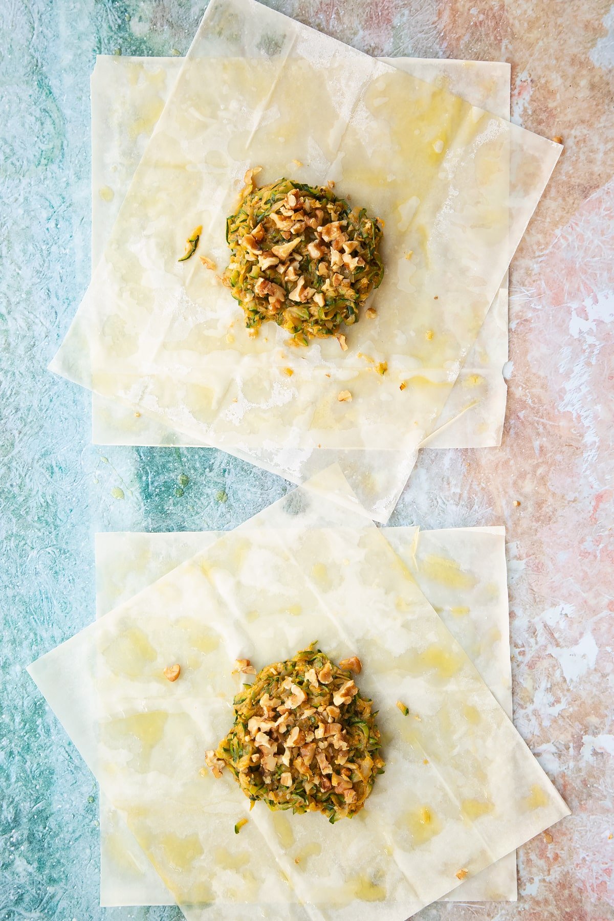 a sheet of filo pastry layered up on a floured surface cut in half with a brush of oil on top, topped with cooked courgette mix.