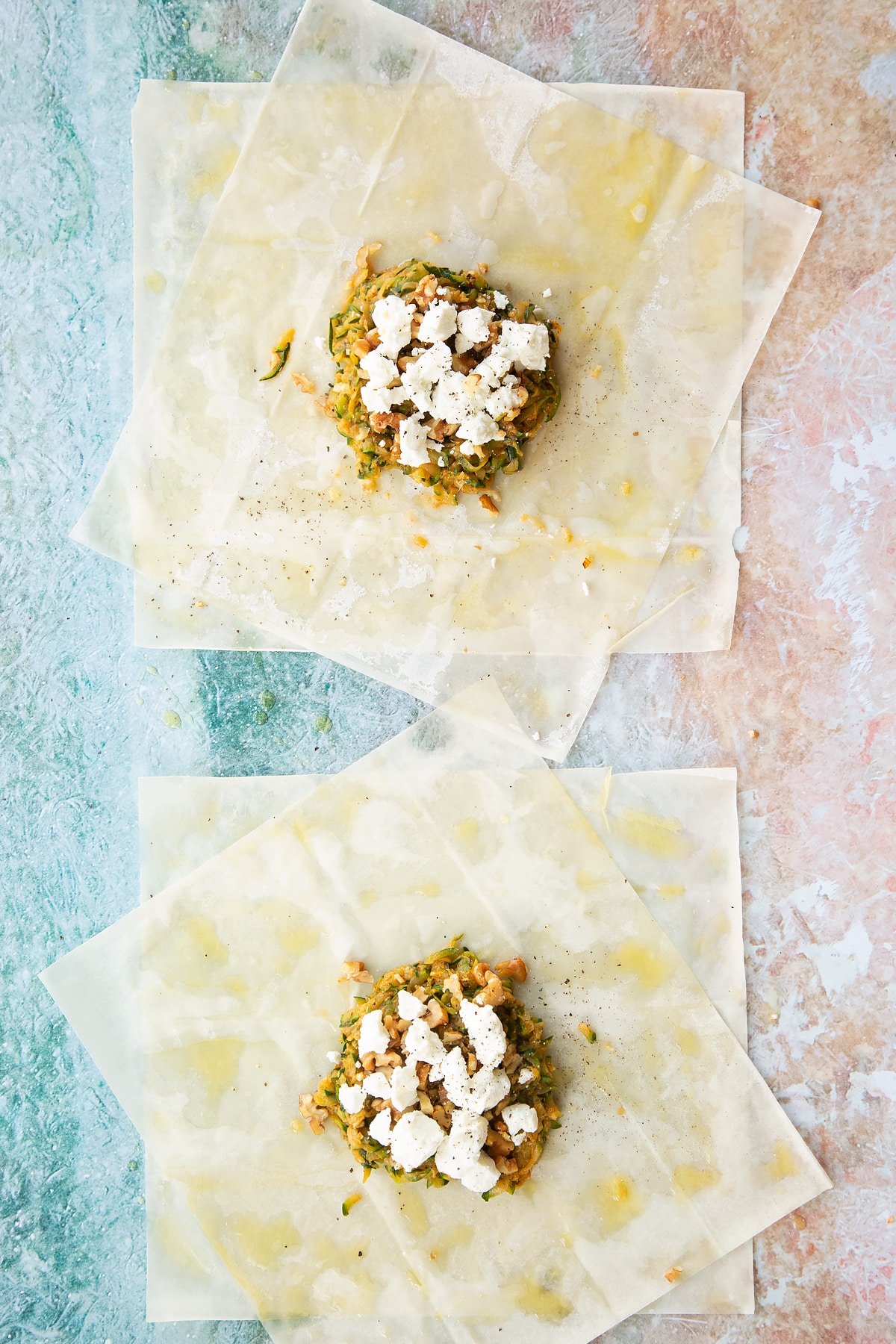 a sheet of filo pastry layered up on a floured surface cut in half with a brush of oil on top, topped with cooked courgette mix and goats cheese.