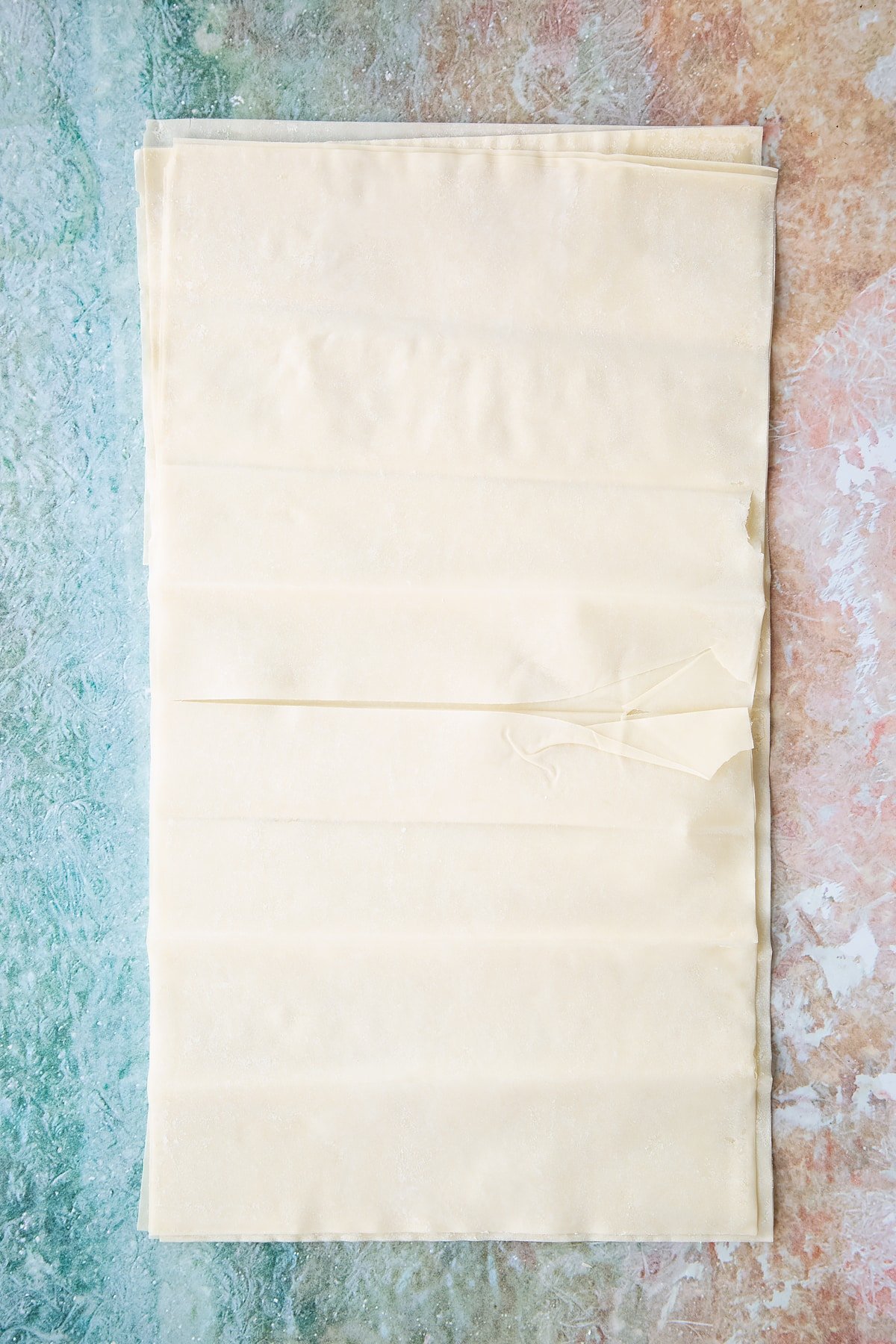 sheets of filo pastry layered up on a floured surface.