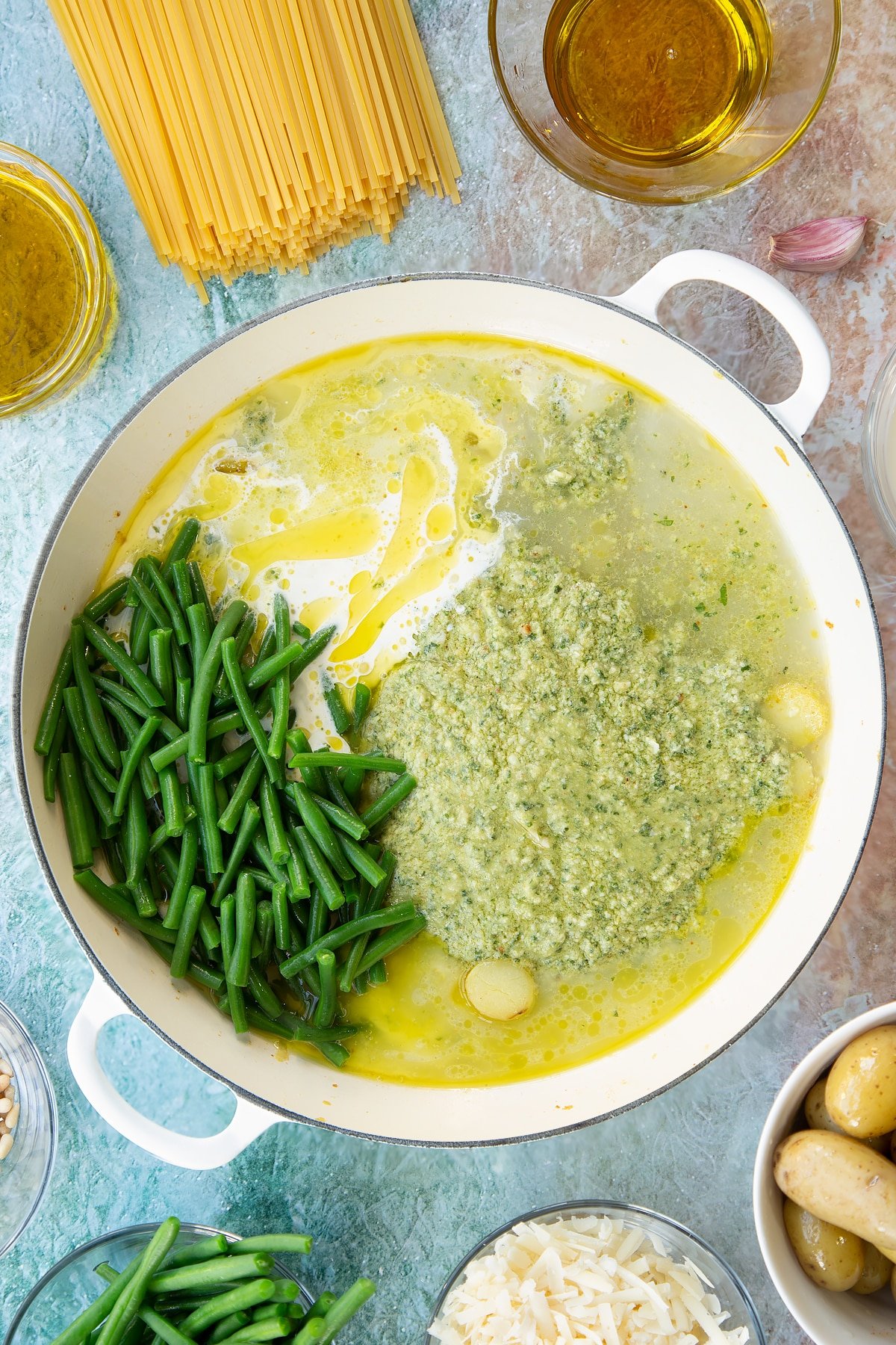 Overhead shot of the potatoes, green beans, pesto and oil in a pan.