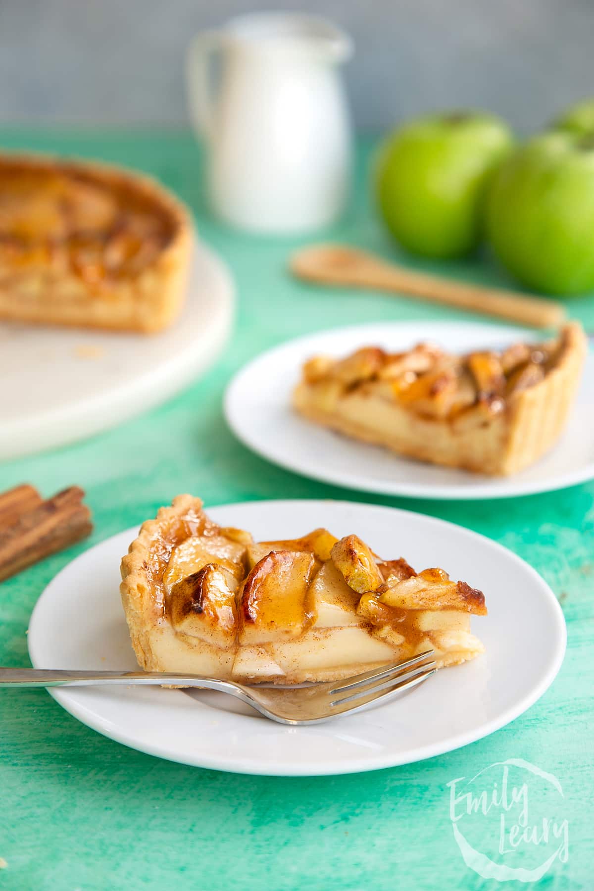 A finished slice of apple custard tart served on a white plate with a fork on the side. 