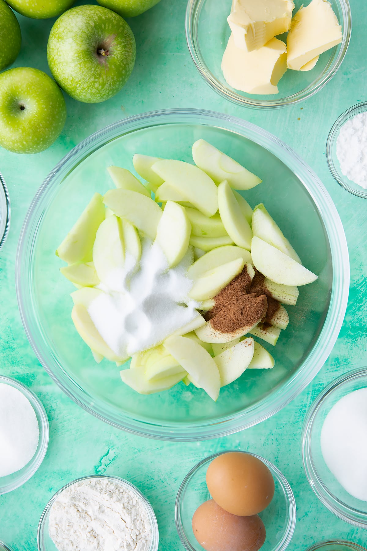 Adding the sugar, cinnamon and lemon juice to the bowl of sliced apples.