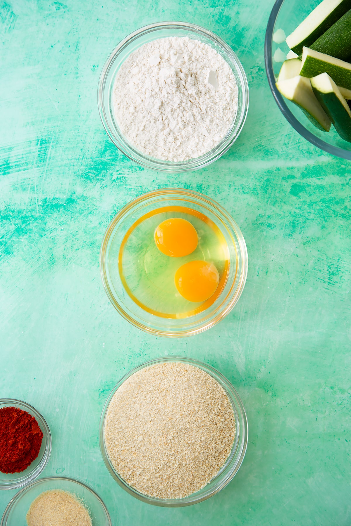 Three mixing bowls, one with flour, one with eggs and one with breadcrumbs