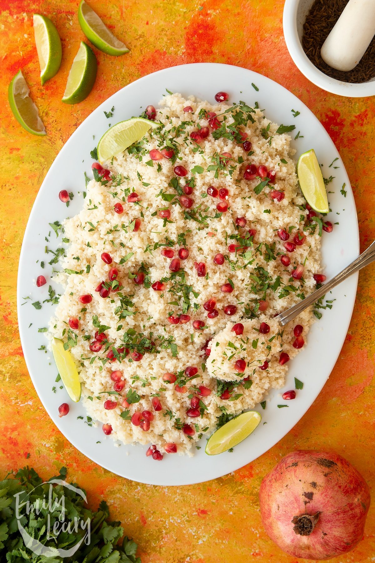 Overhead shot of the finished cauliflower couscous with pomegranate served on a white plate. 