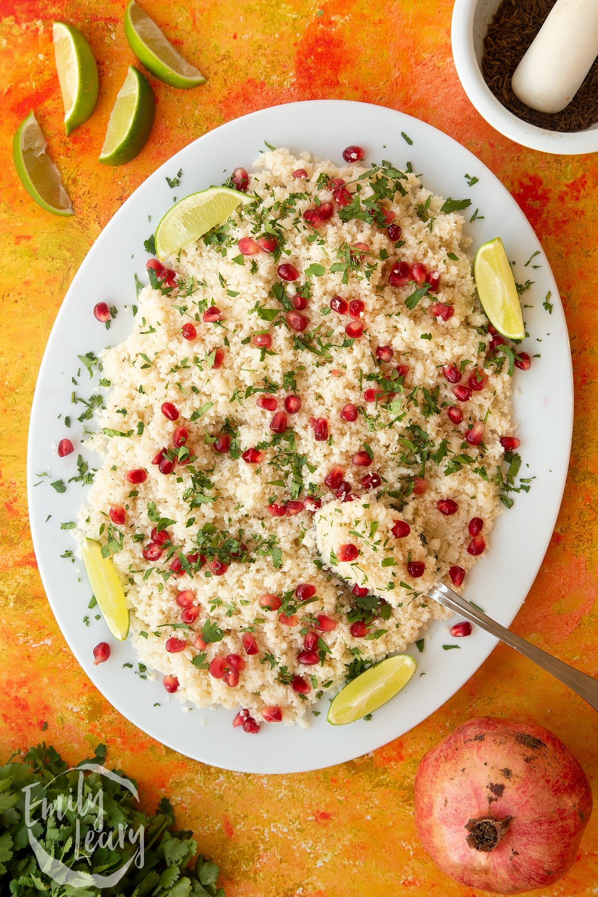 Overhead shot of cauliflower couscous with pomegranate served on a white plate.