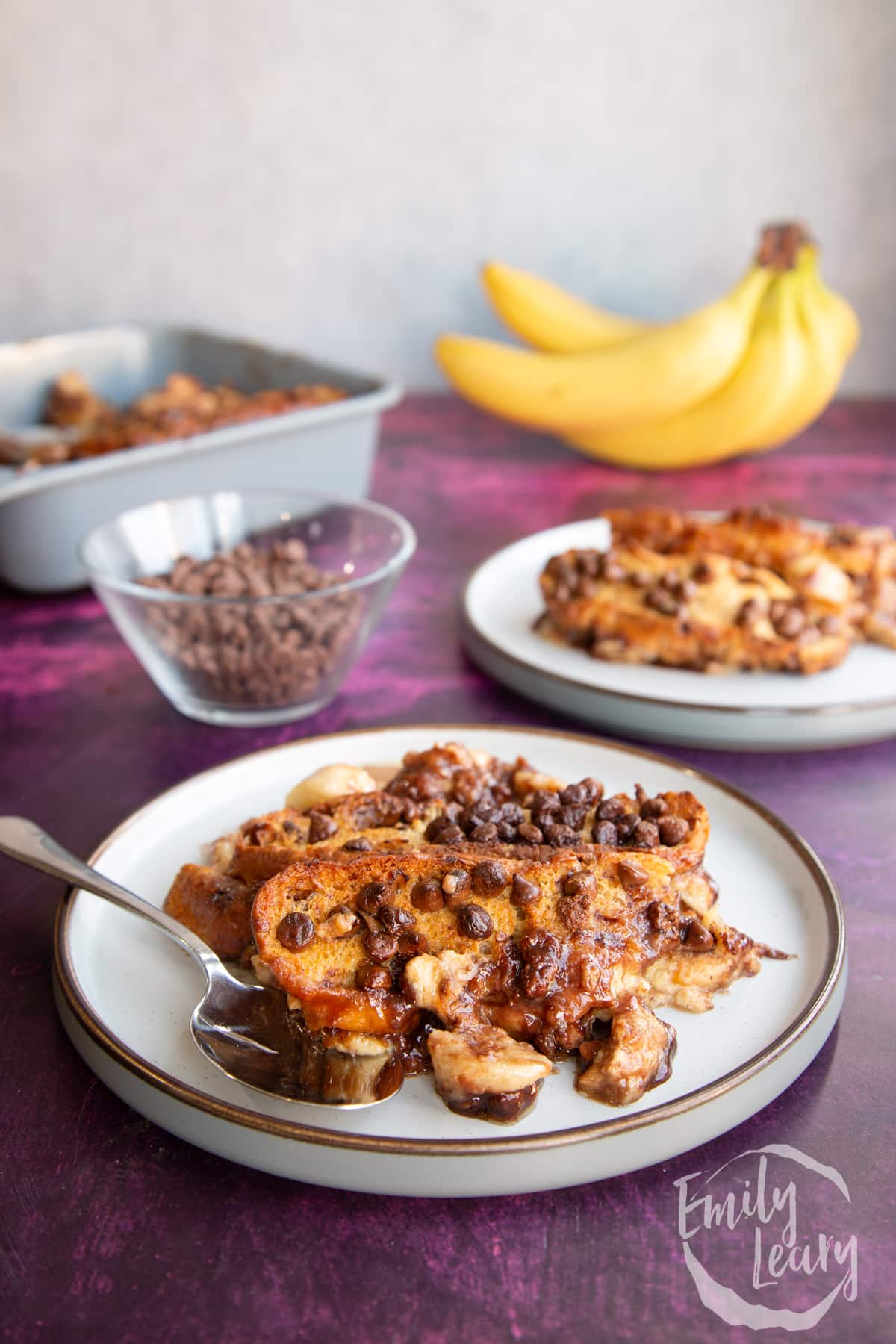 Chocolate banana bread pudding served on a decorative plate with a spoon on the side.