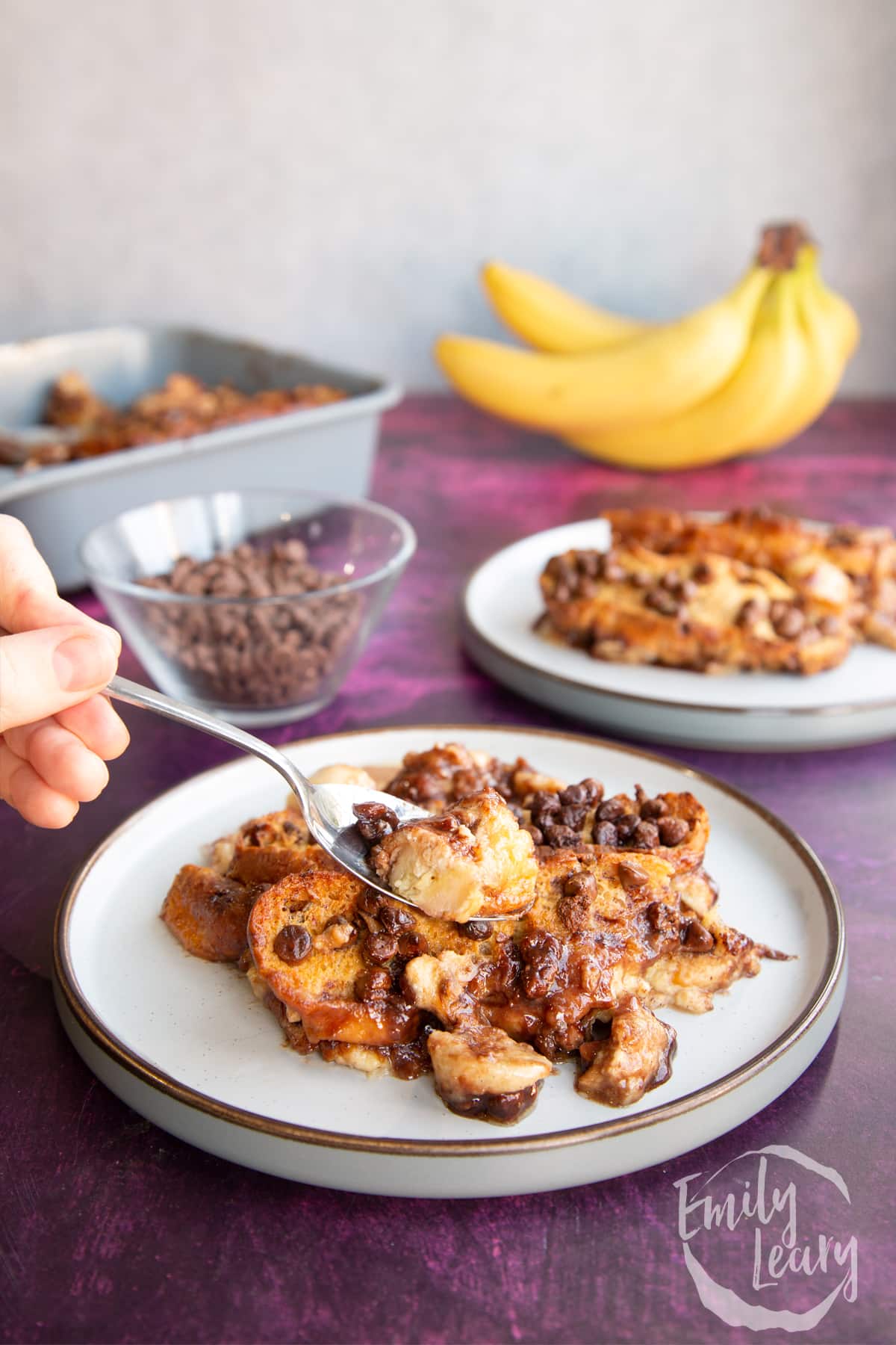 A spoon going into the serving of chocolate banana bread pudding.