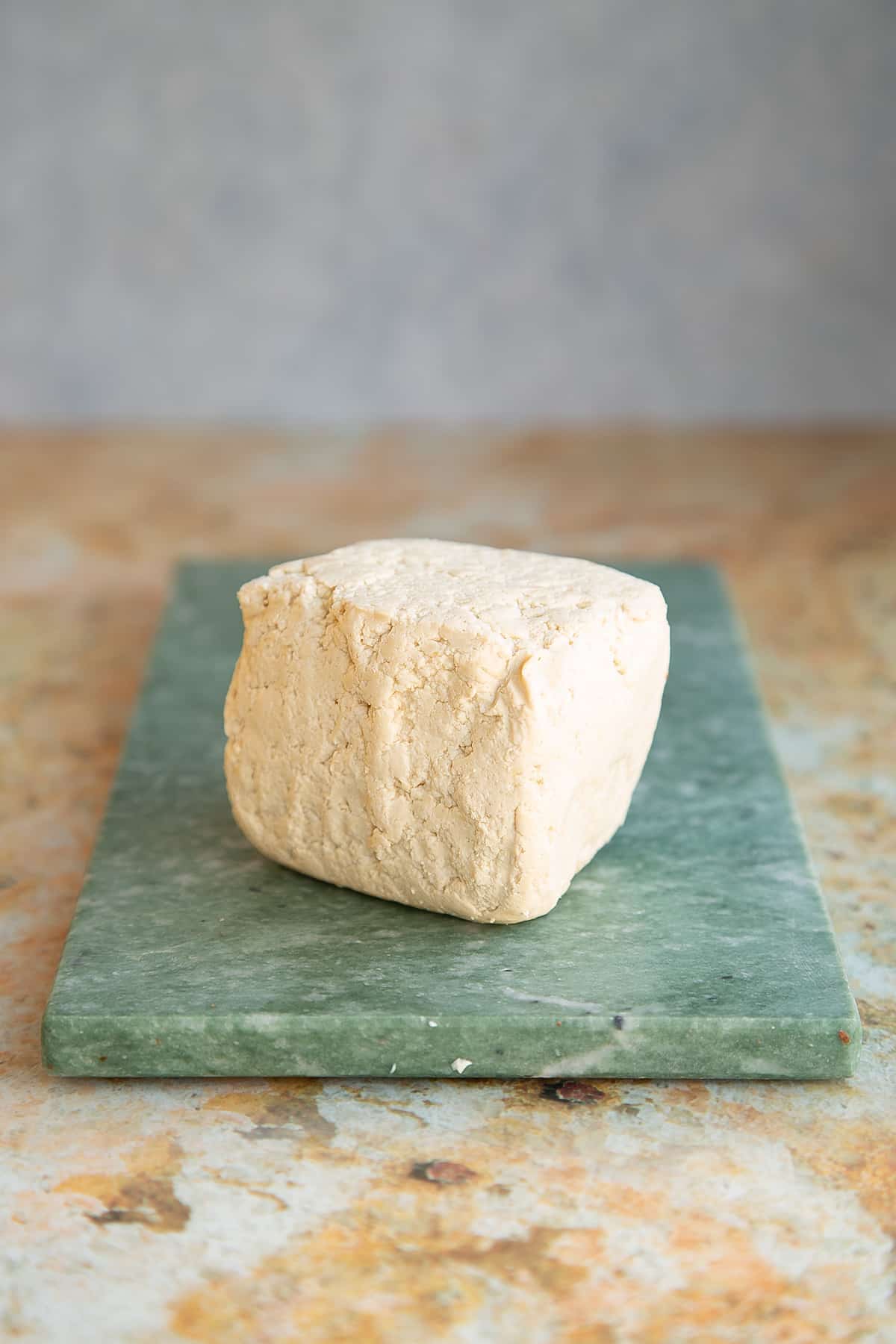 a block of extra firm tofu on a green marble chopping board.